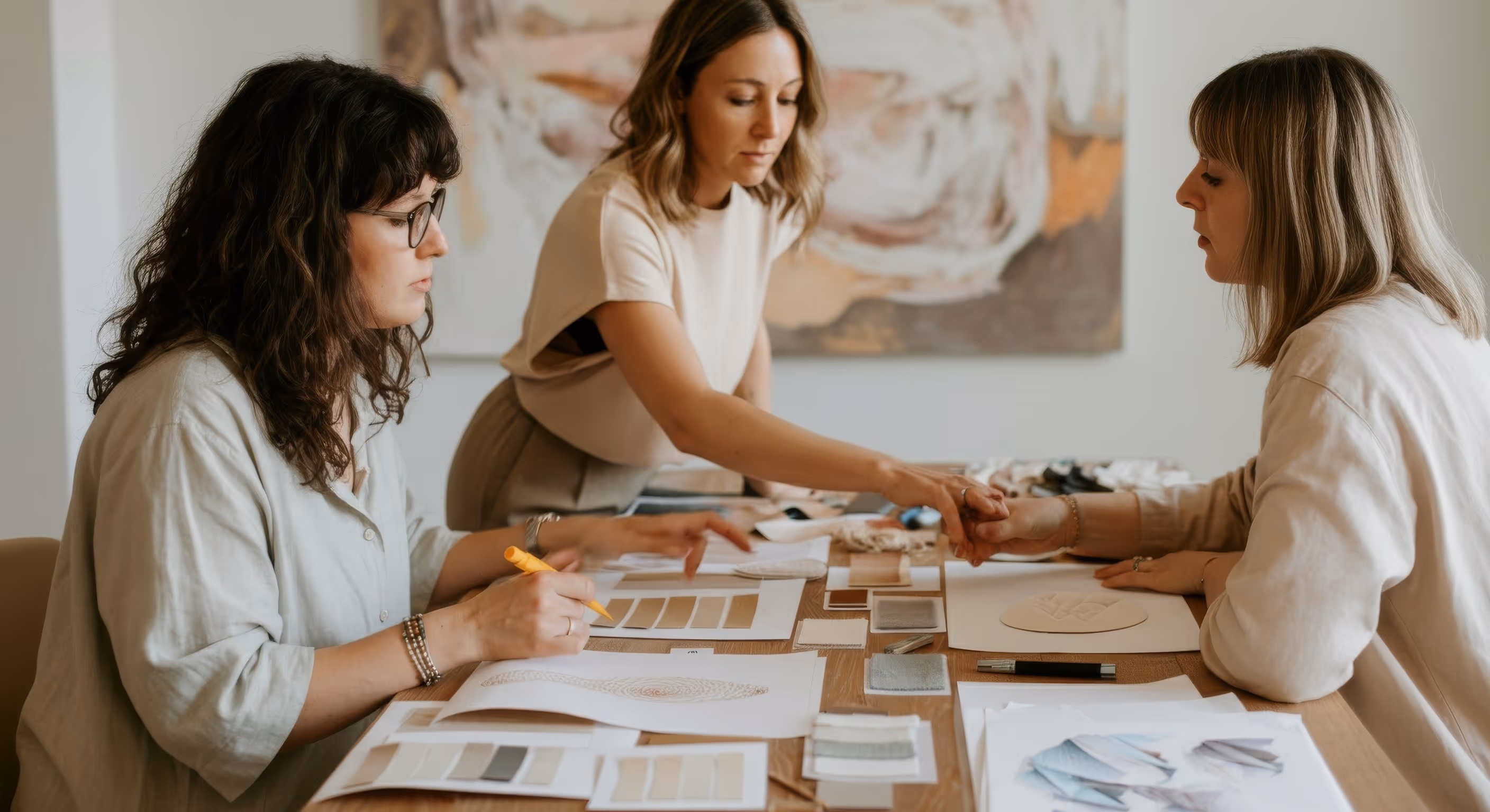 Three women collaborating at a table with color swatches and design sketches.
