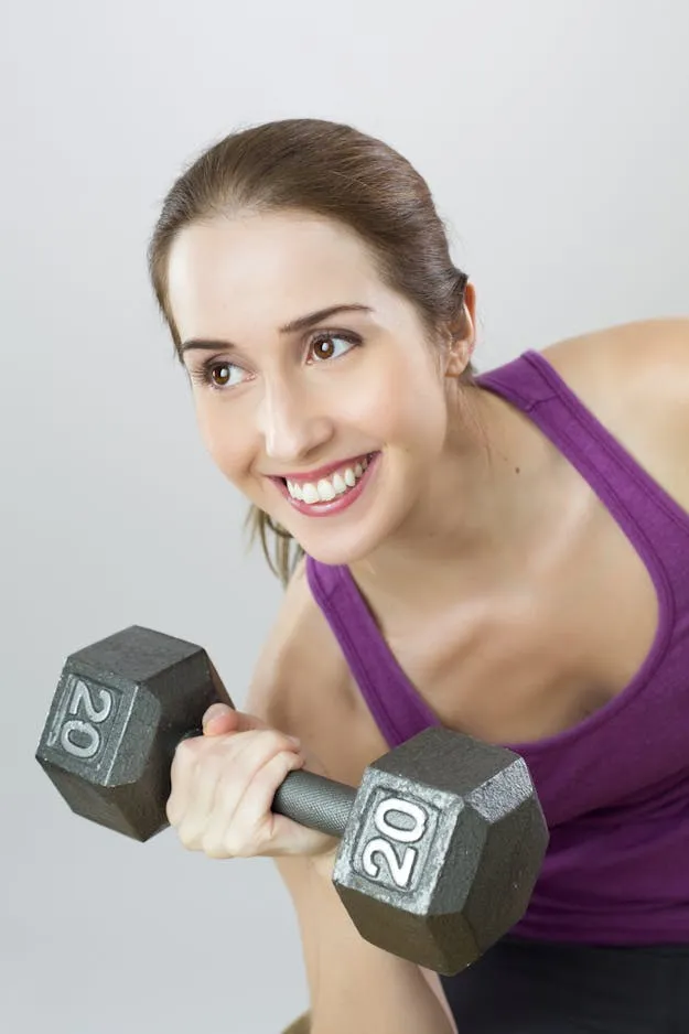 A woman is smiling while holding two dumbs.