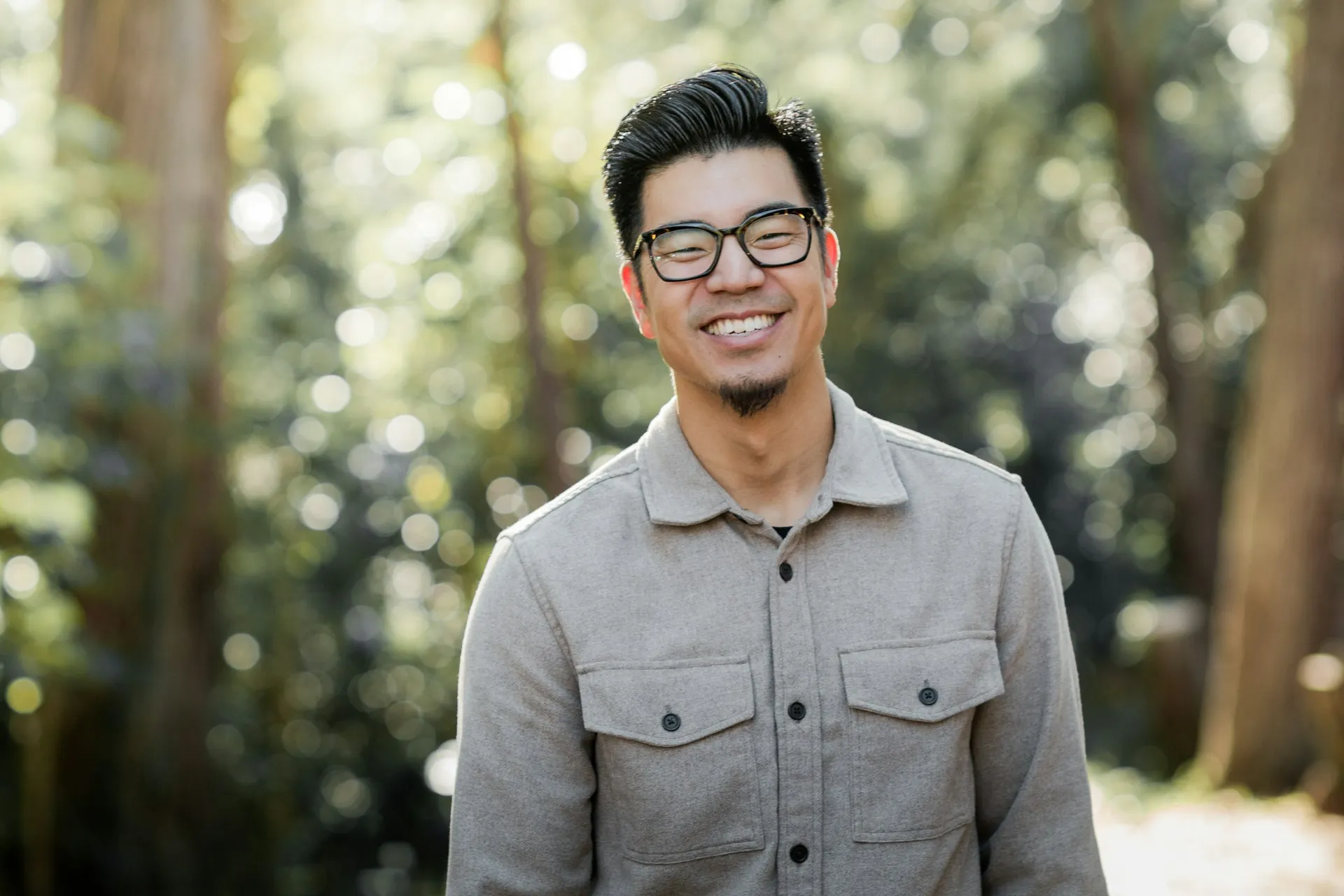 A man wearing glasses standing in front of trees.