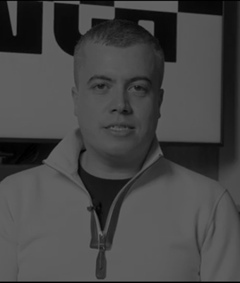 Man with short hair wearing a light-colored zip-up sweater, sitting indoors in front of a partially visible sign.