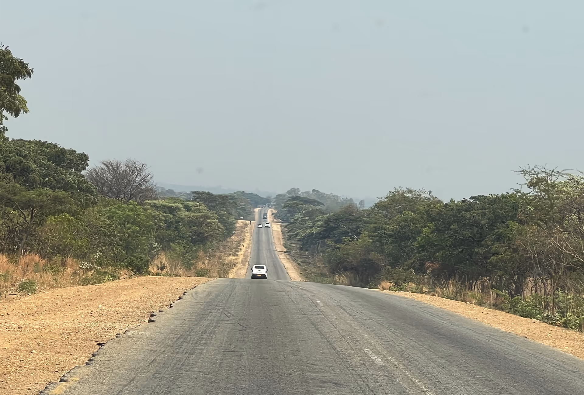 Fahrt durch das ländliche Hinterland von Zimbabwe mit Blick auf Strasse und bewaldete Hügellandschaft.