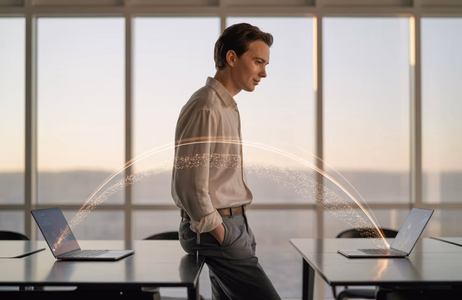 Man leaning on a table in an office with digital light arcs connecting two laptops.
