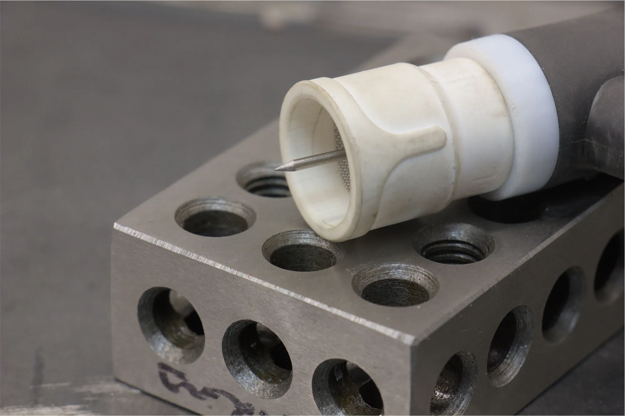 Close-up of a TIG welding torch tip and tungsten electrode resting on a precision machined setup block, highlighting Flatirons Rapid Prototyping's integrated welding and fabrication capabilities.