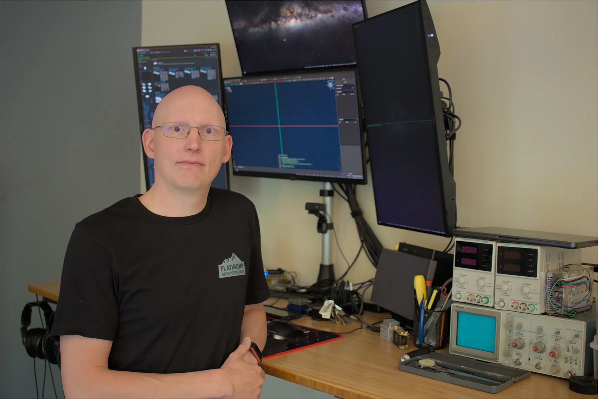 Keven Wyld, Founder of Flatirons Rapid Prototyping, standing in his office surrounded by engineering monitors and electronic test equipment, highlighting his background in design support and technical problem-solving.
