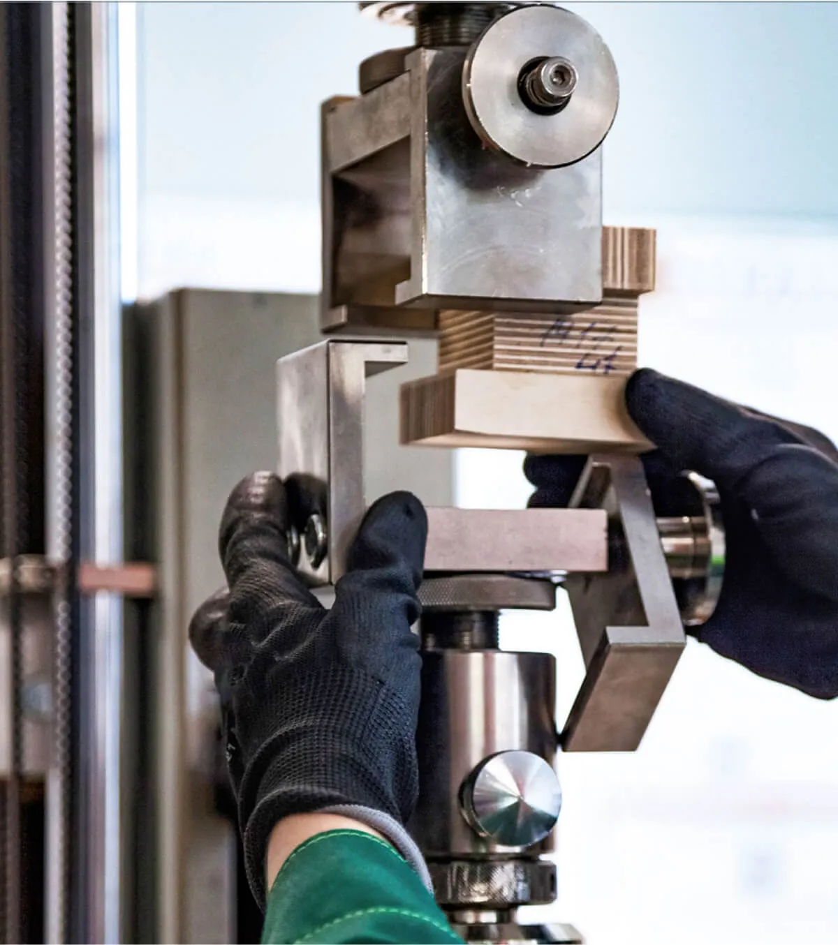 Gloved hands of a technician setting a precision-machined prototype part into a metal testing or quality control fixture.