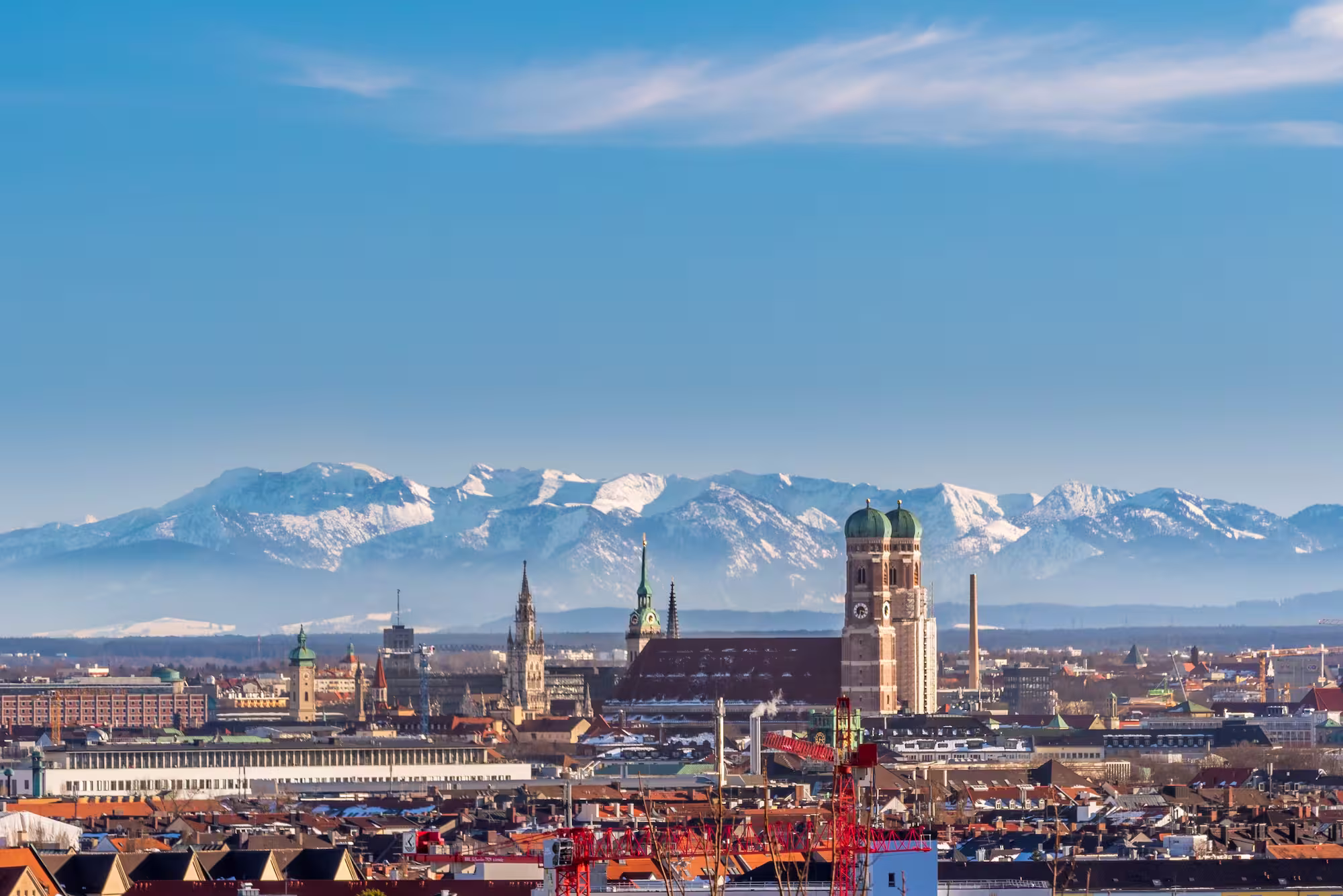 Stadt München vor schneebedeckten Alpen unter blauem Himmel.