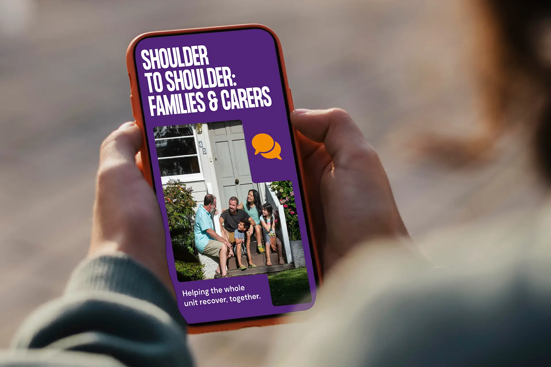 A person holding a phone displaying the Shoulder to Shoulder: Families & Carers program screen.