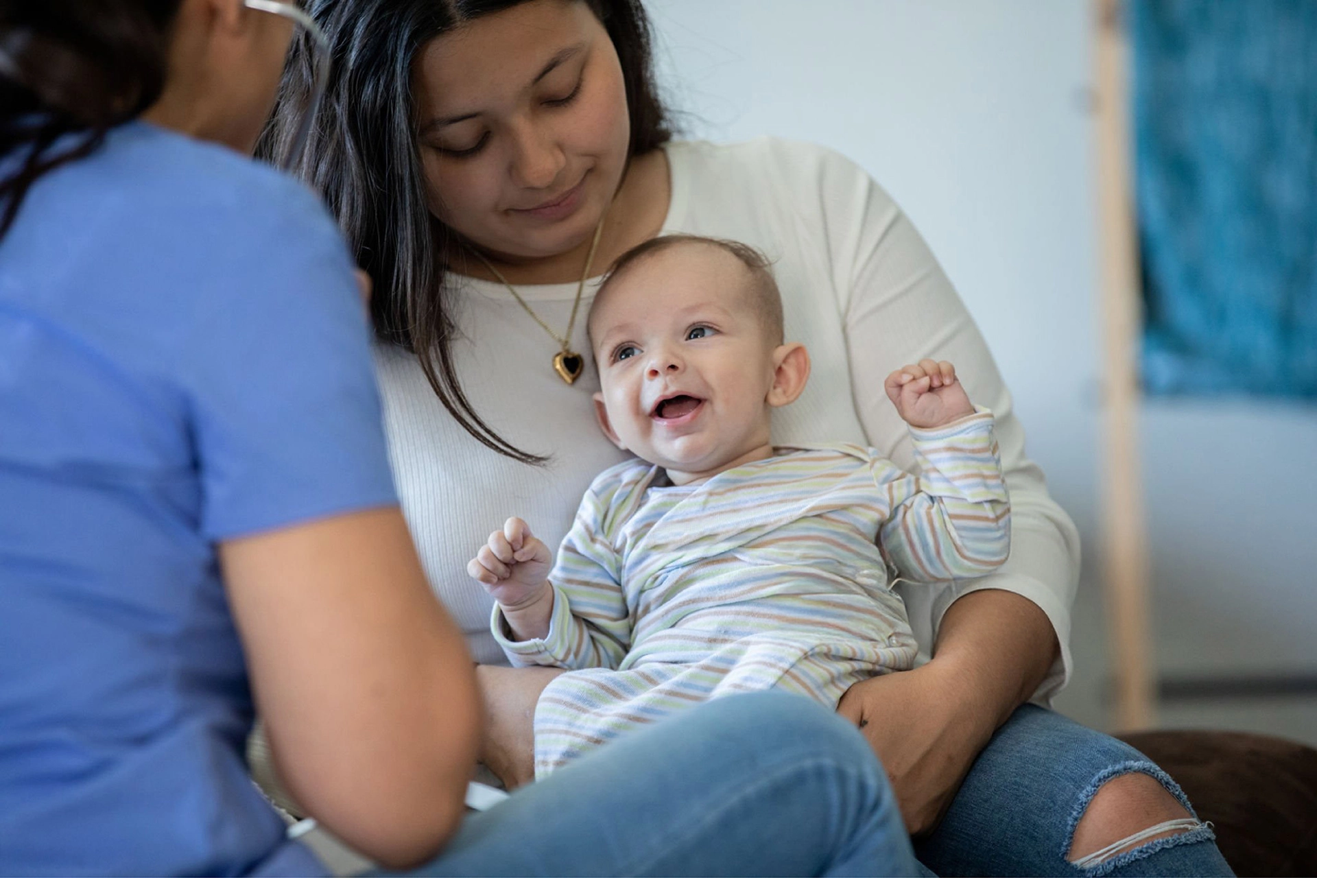 Parent holding a smiling baby while speaking with a healthcare worker.