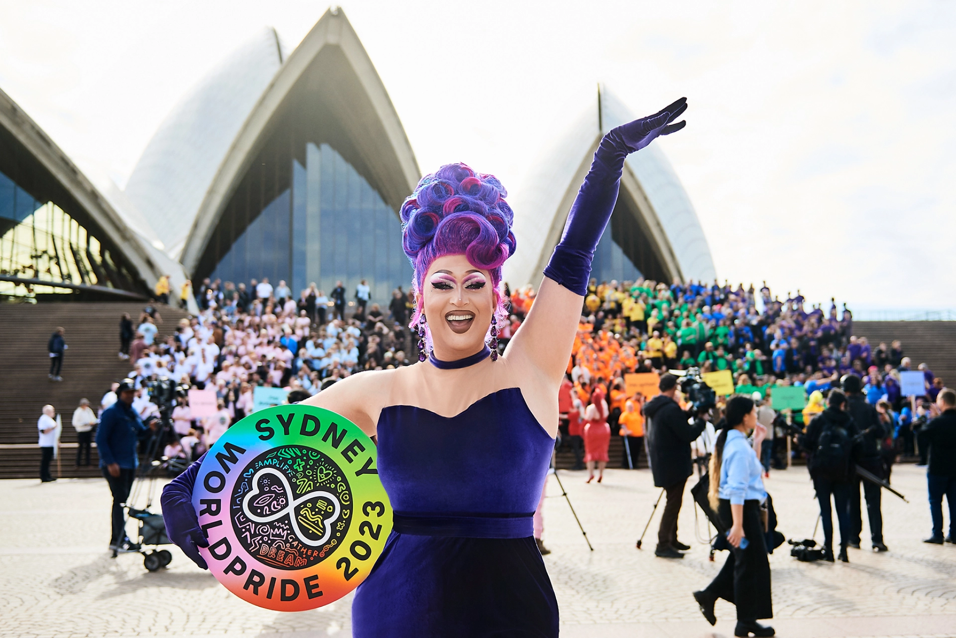 Pride attendee posing with a rainbow fan outside the Sydney Opera House during WorldPride celebrations.