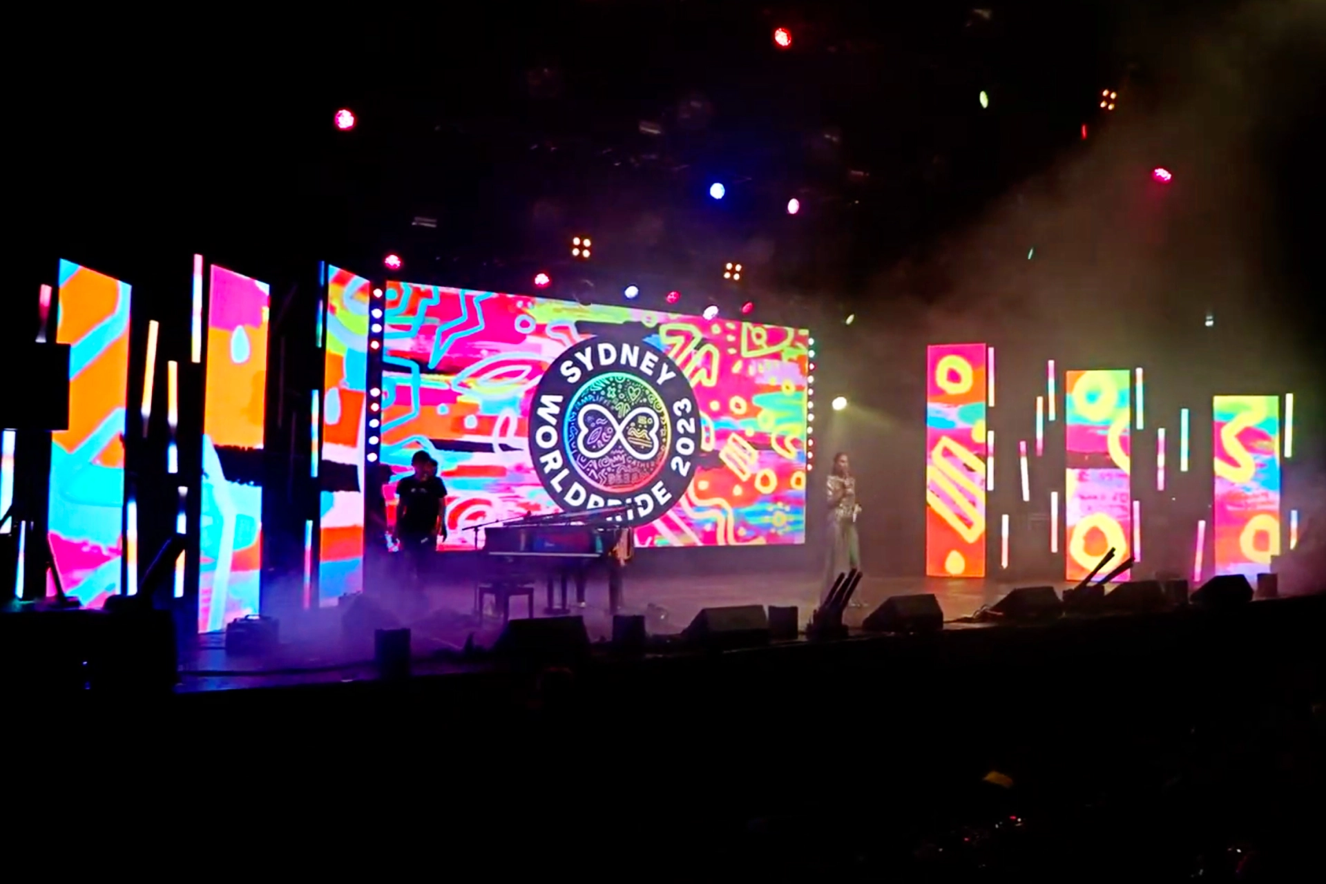 Stage lit with rainbow colours during a WorldPride performance, with screens showing Pride-themed visuals.