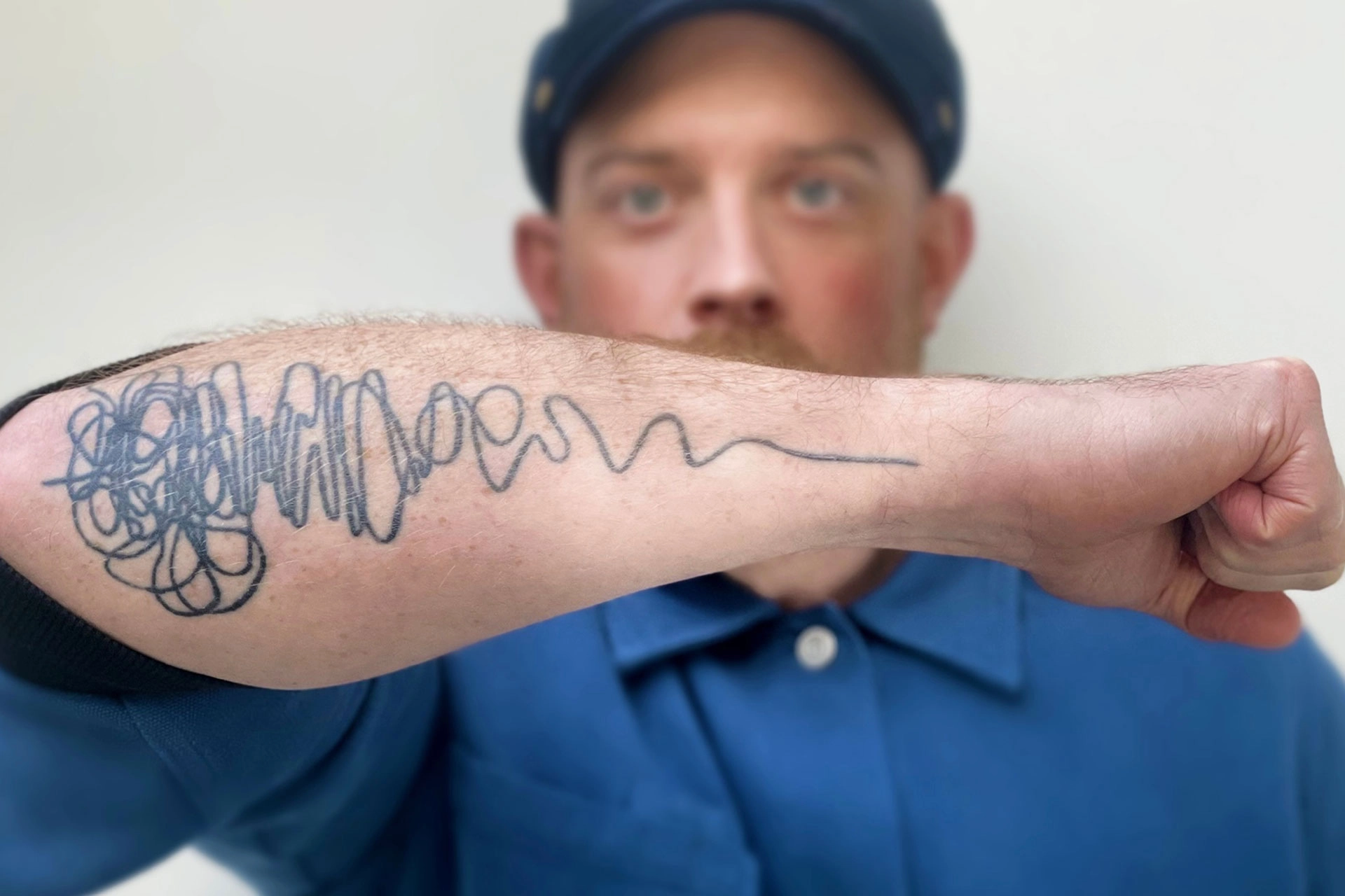 Man holding out his arm to show a tattoo of a squiggly line, representing the non-linear design process.