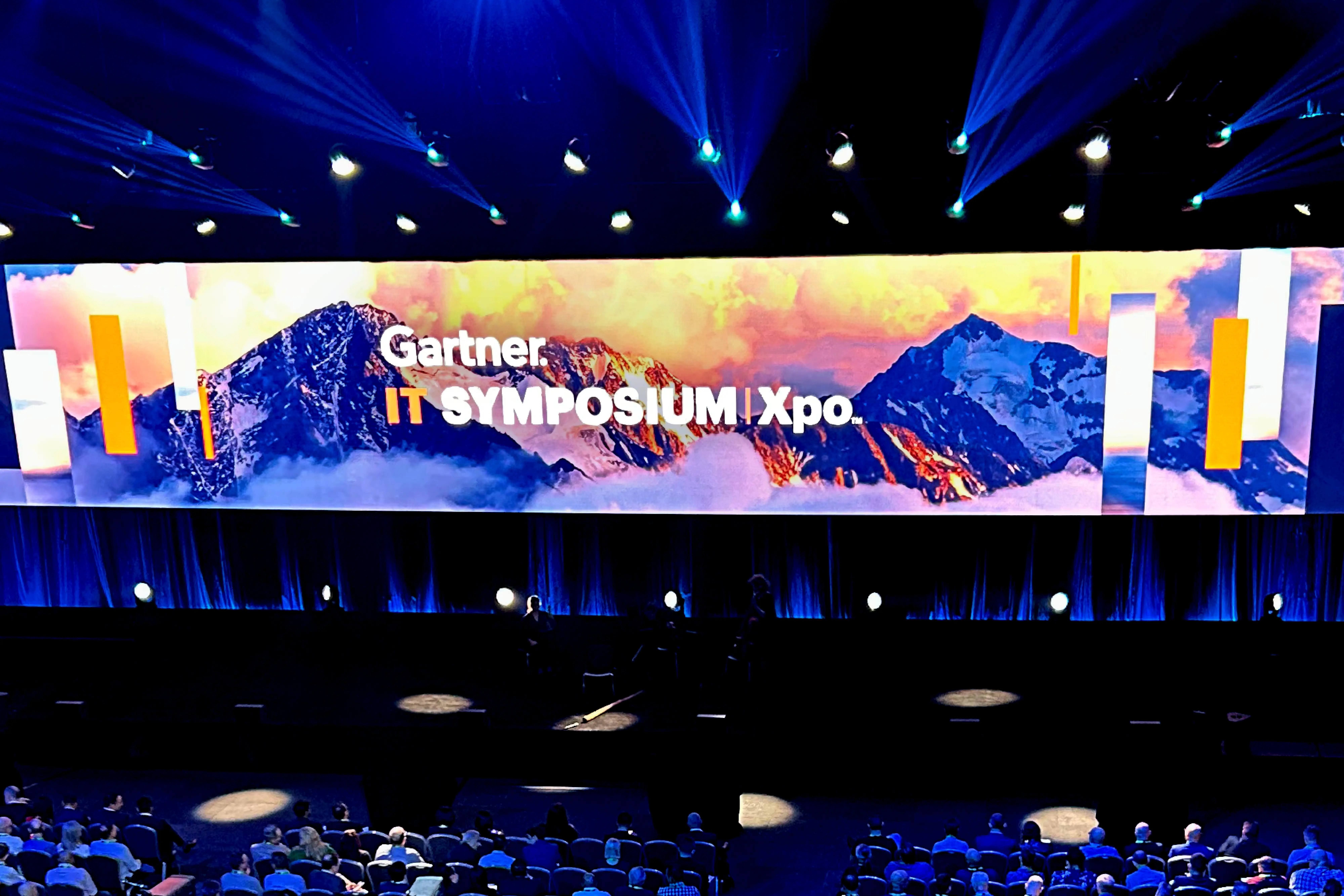 A wide shot of the Gartner IT Symposium 2023 main stage with bright digital displays and an audience.
