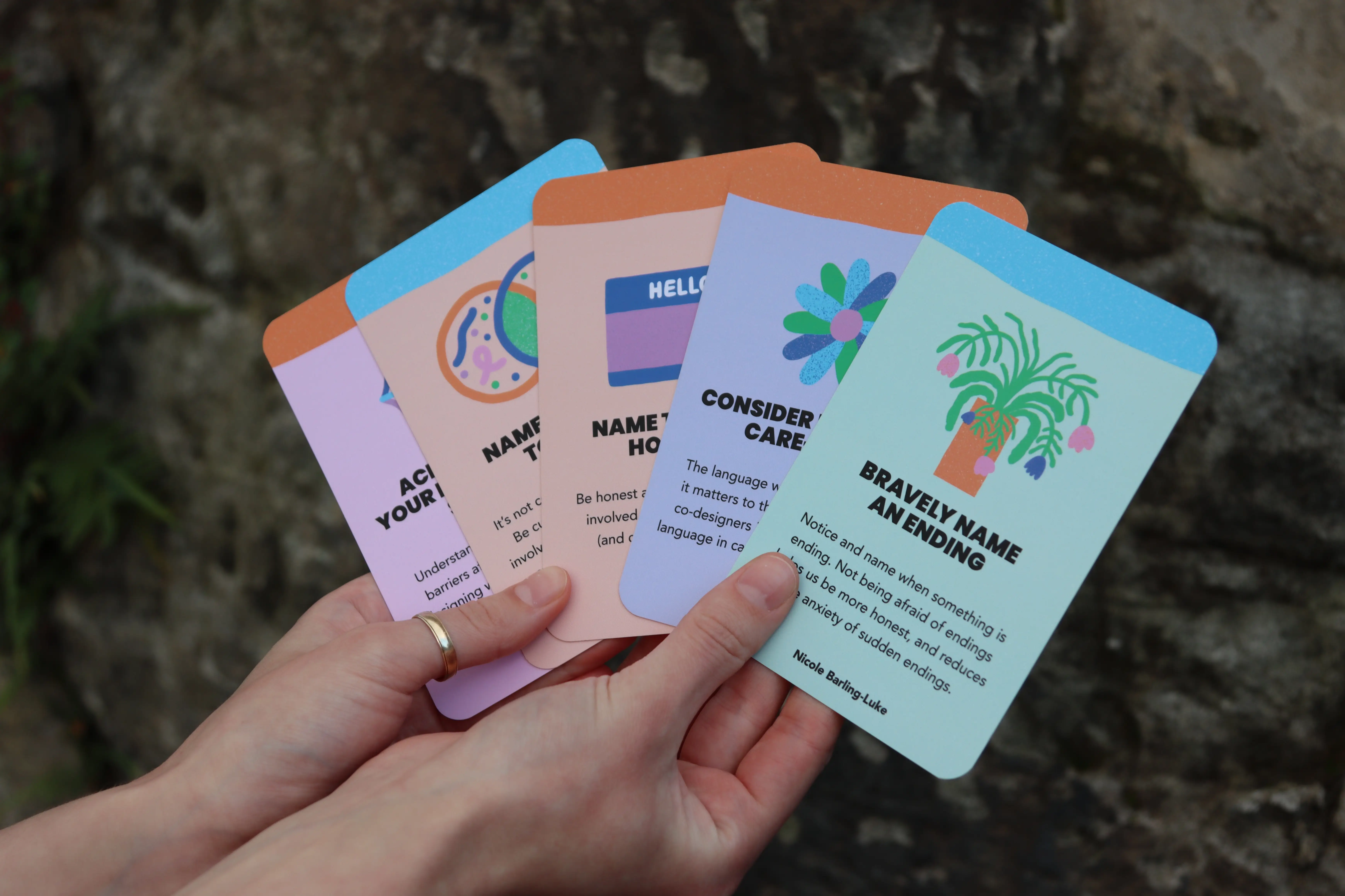 A hand fanning out several cards from the new Beyond Sticky Notes Model of Care for Co-design Expansion Pack, showing illustrated prompts designed to support inclusive, values-led co-design.