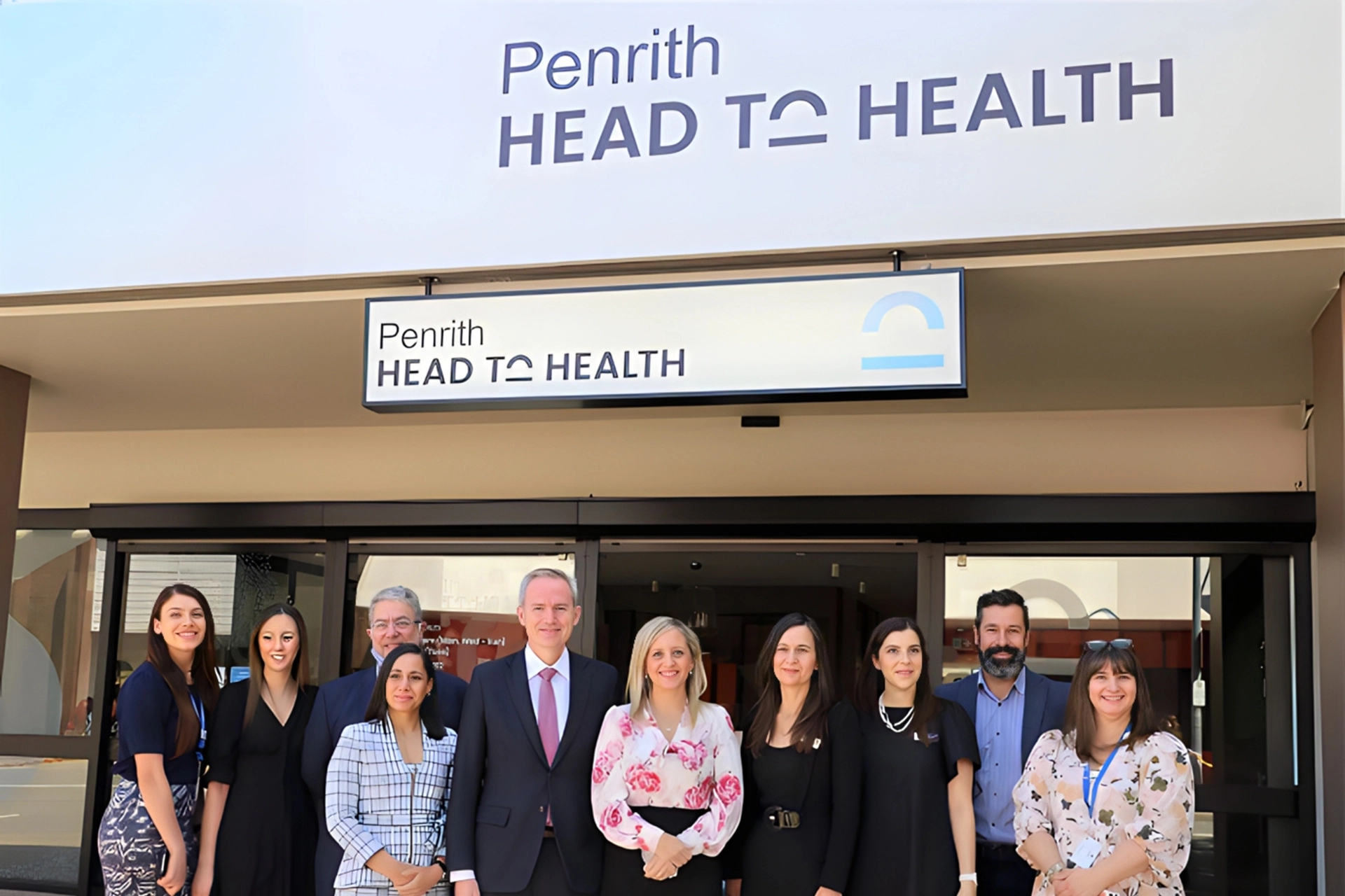 Group of Neami National staff and officials standing outside the Penrith Head to Health centre beneath the centre’s signage.