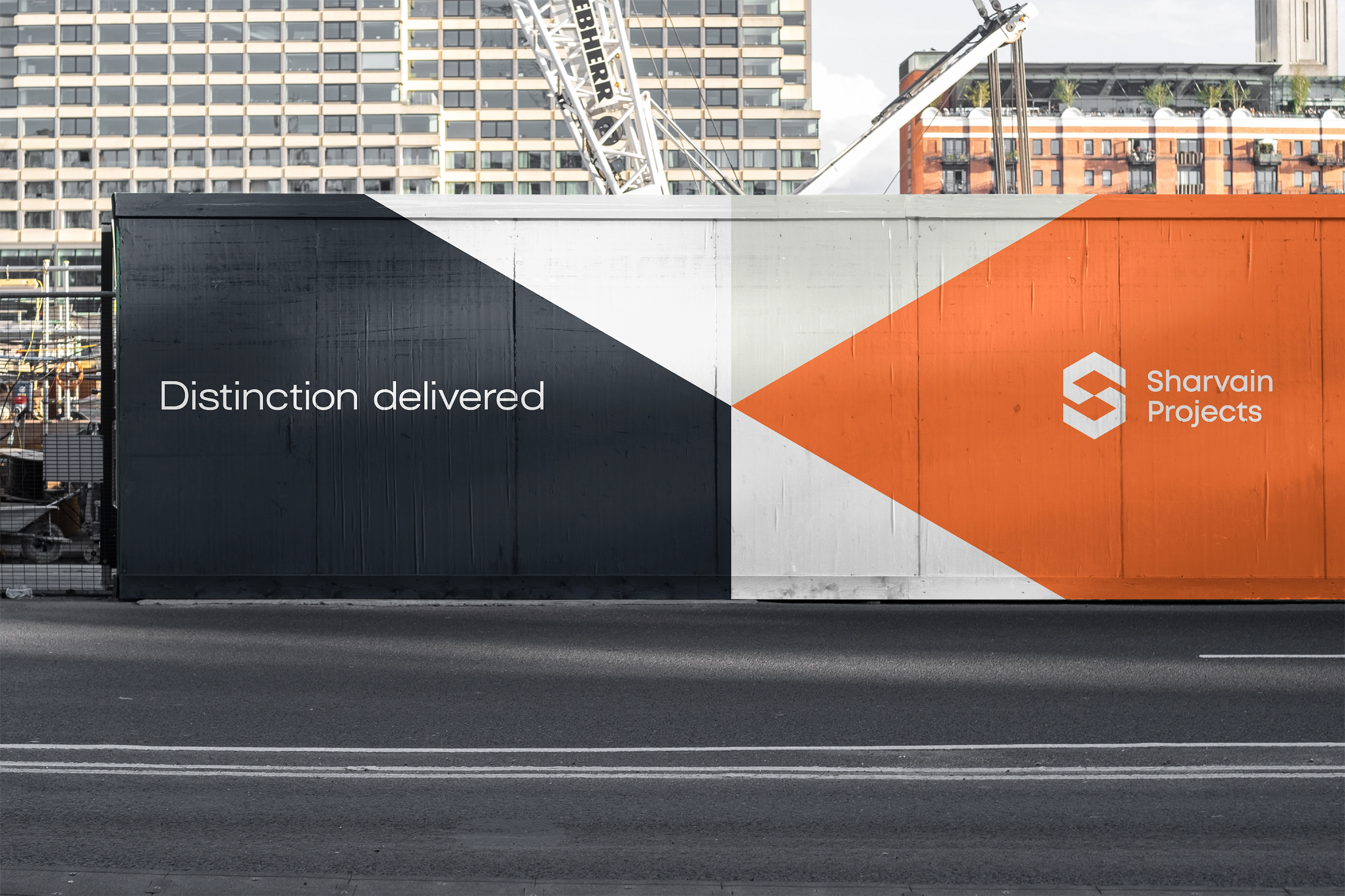 Large construction site hoarding featuring Sharvain Projects branding and geometric shapes with the tagline “Distinction delivered.”