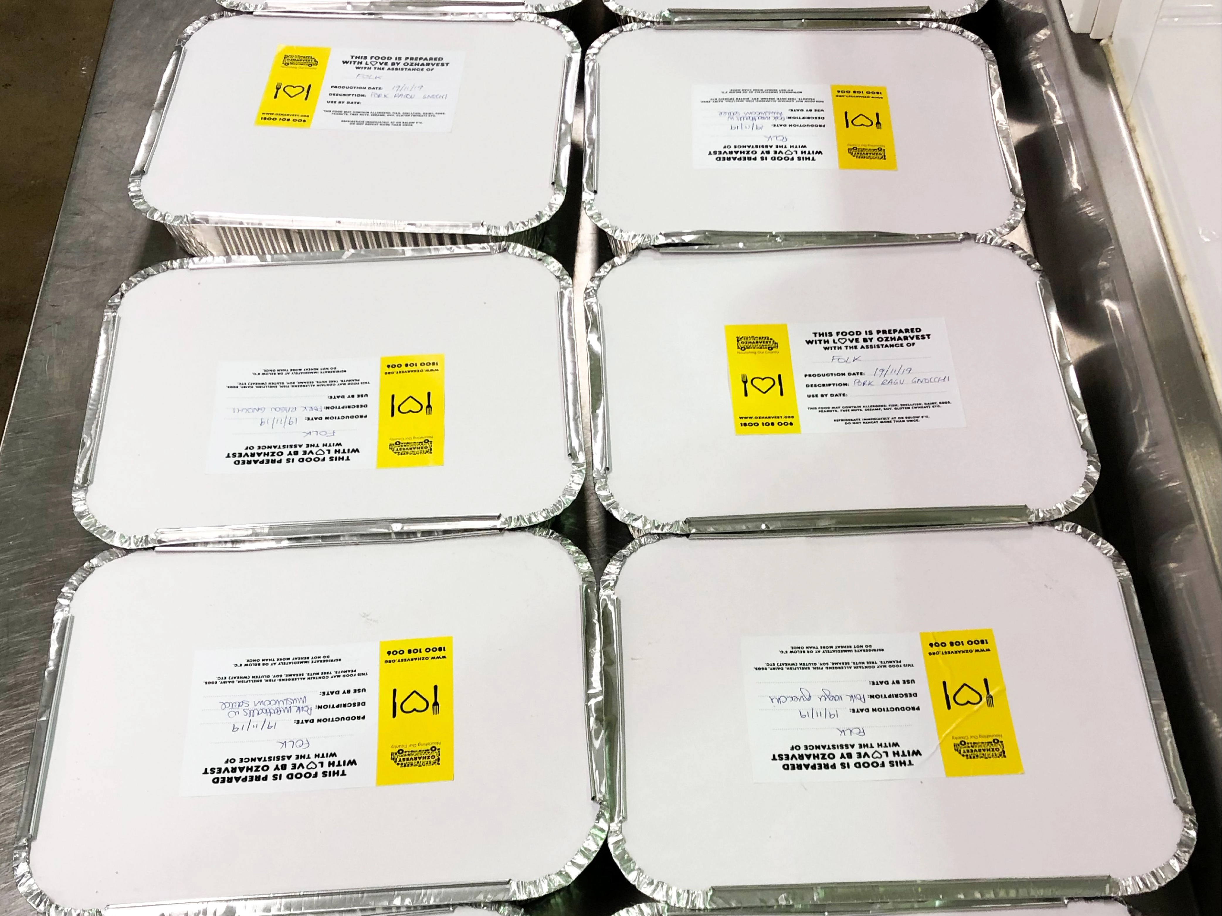 Multiple sealed food trays labelled with OzHarvest and Folk branding ready for distribution.