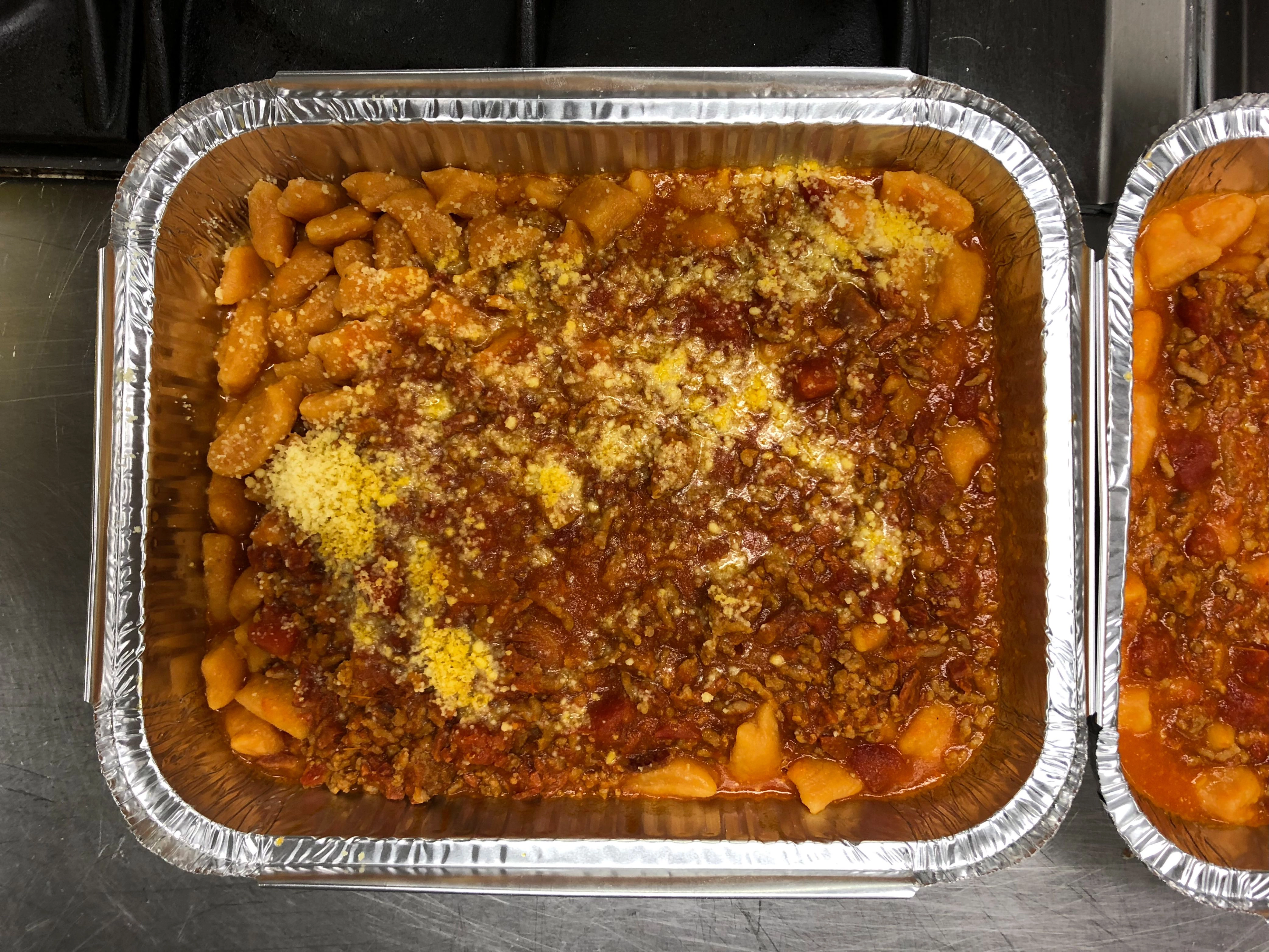 Tray of cooked gnocchi in tomato and mince sauce topped with cheese.