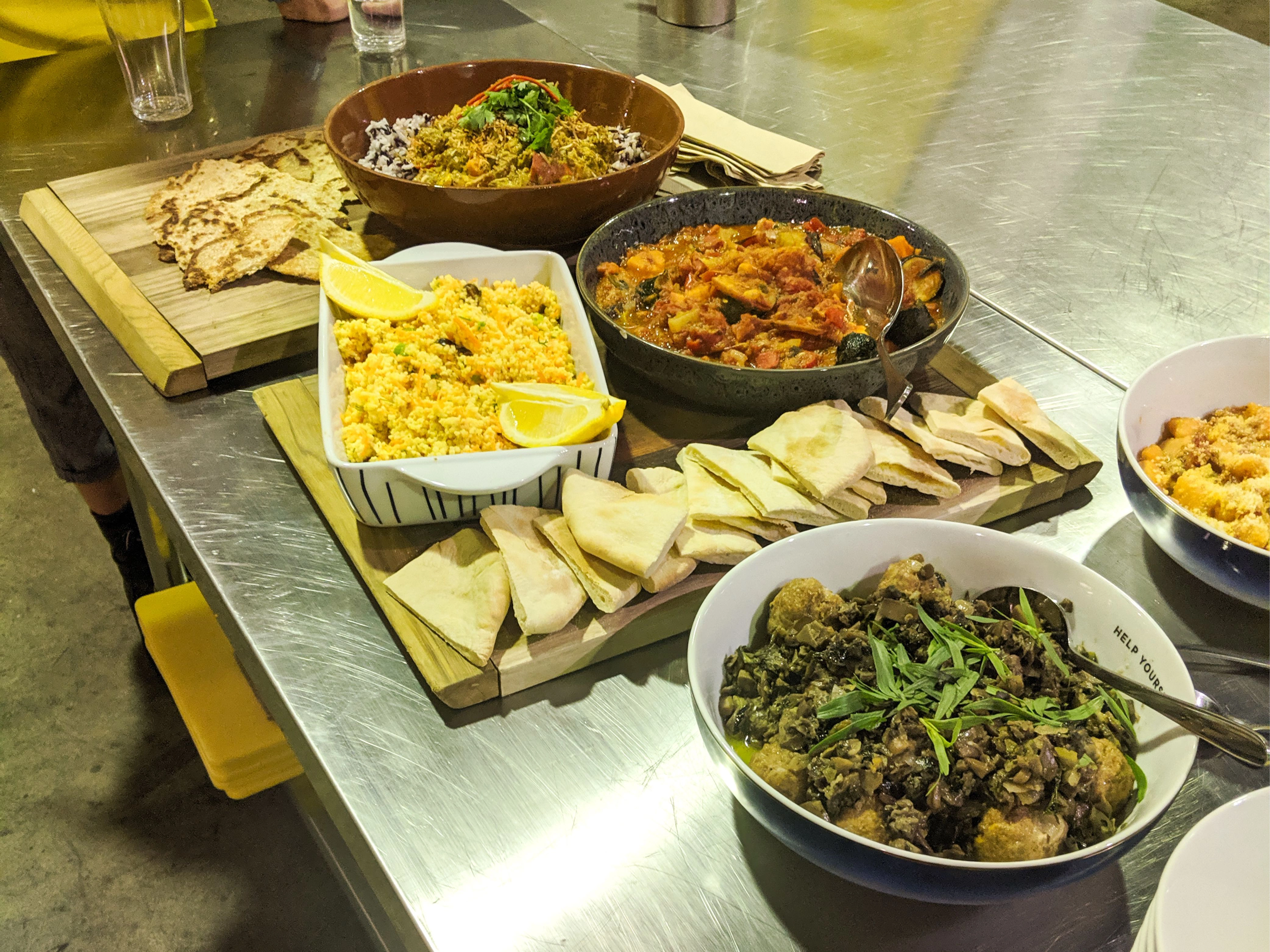 A table of completed dishes including couscous, pita bread, stews and salads prepared during the Cooking for a Cause session.