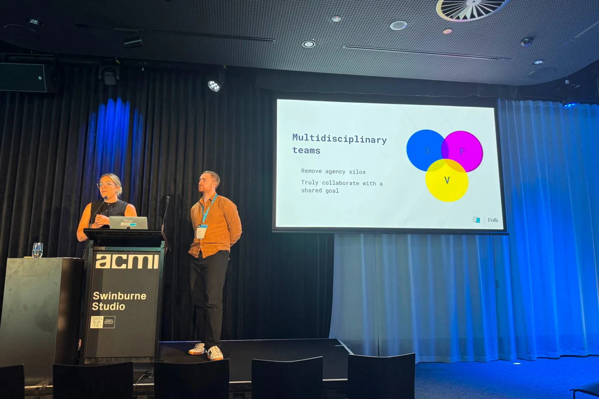 Presenters on stage at DrupalSouth 2023 showing a slide about multi-agency collaboration.