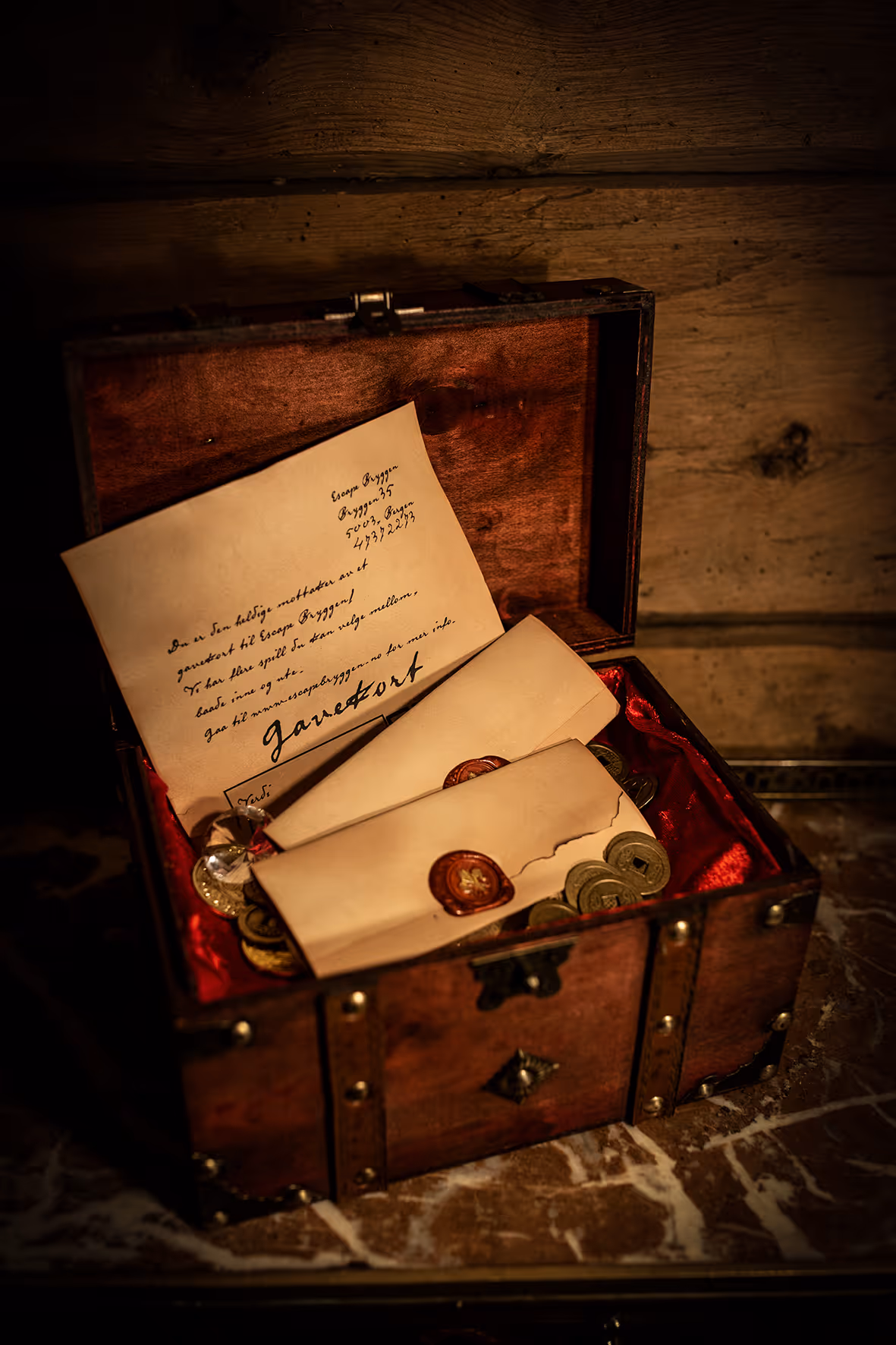 Open wooden chest lined with red fabric containing sealed envelopes, coins, and a handwritten letter.
