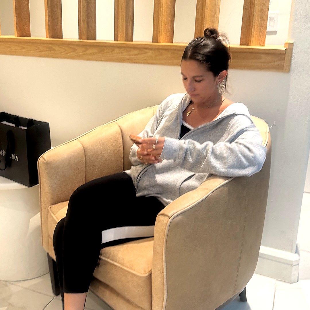 A woman sitting alone in the Materna waiting area, looking at her phone