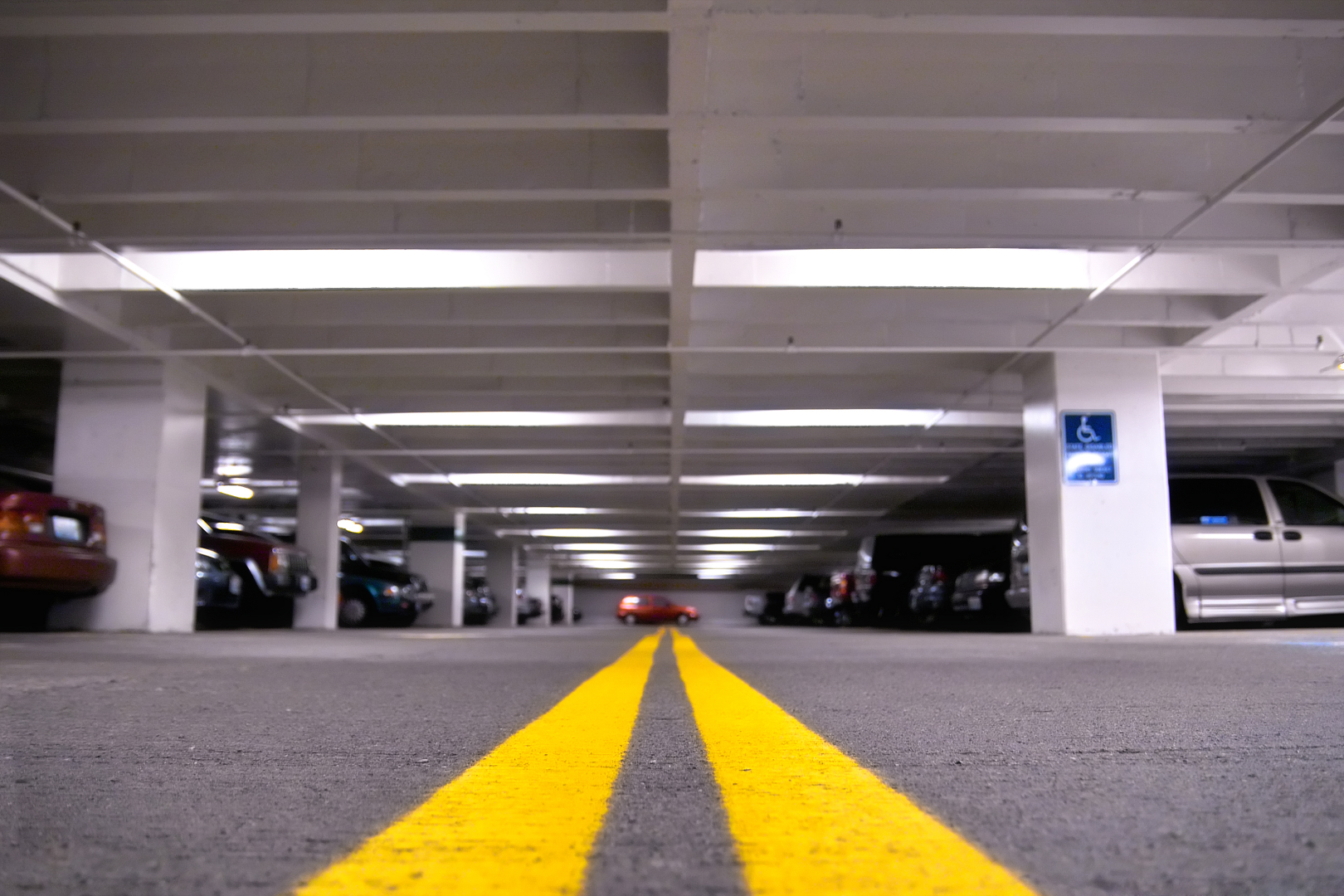 Interior view of a parking garage with bright yellow double lines on the floor and parked cars along the sides.
