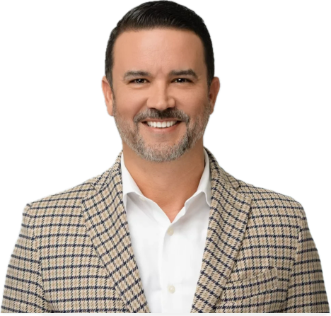 Smiling man with short dark hair and beard wearing a checked blazer over a white shirt.