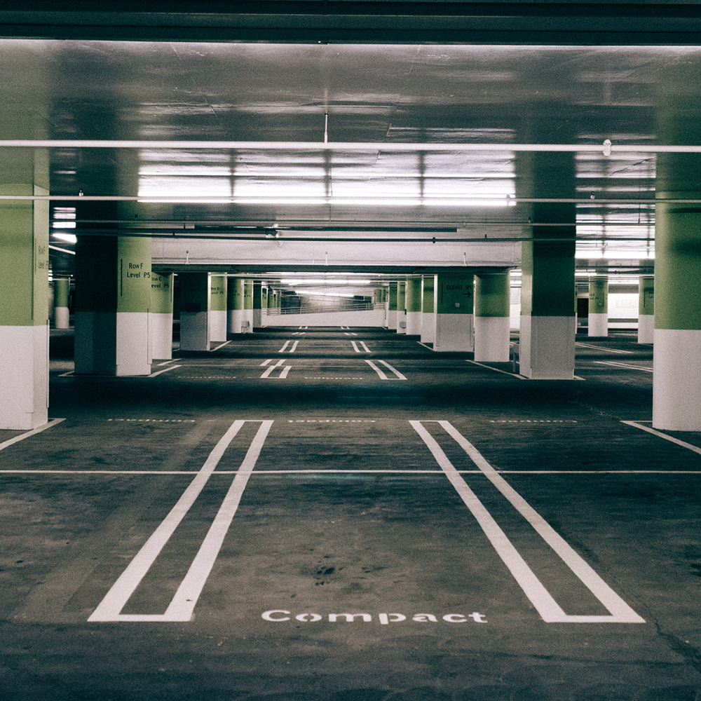 Empty indoor parking garage with green and white pillars and white lines marking compact car spaces.