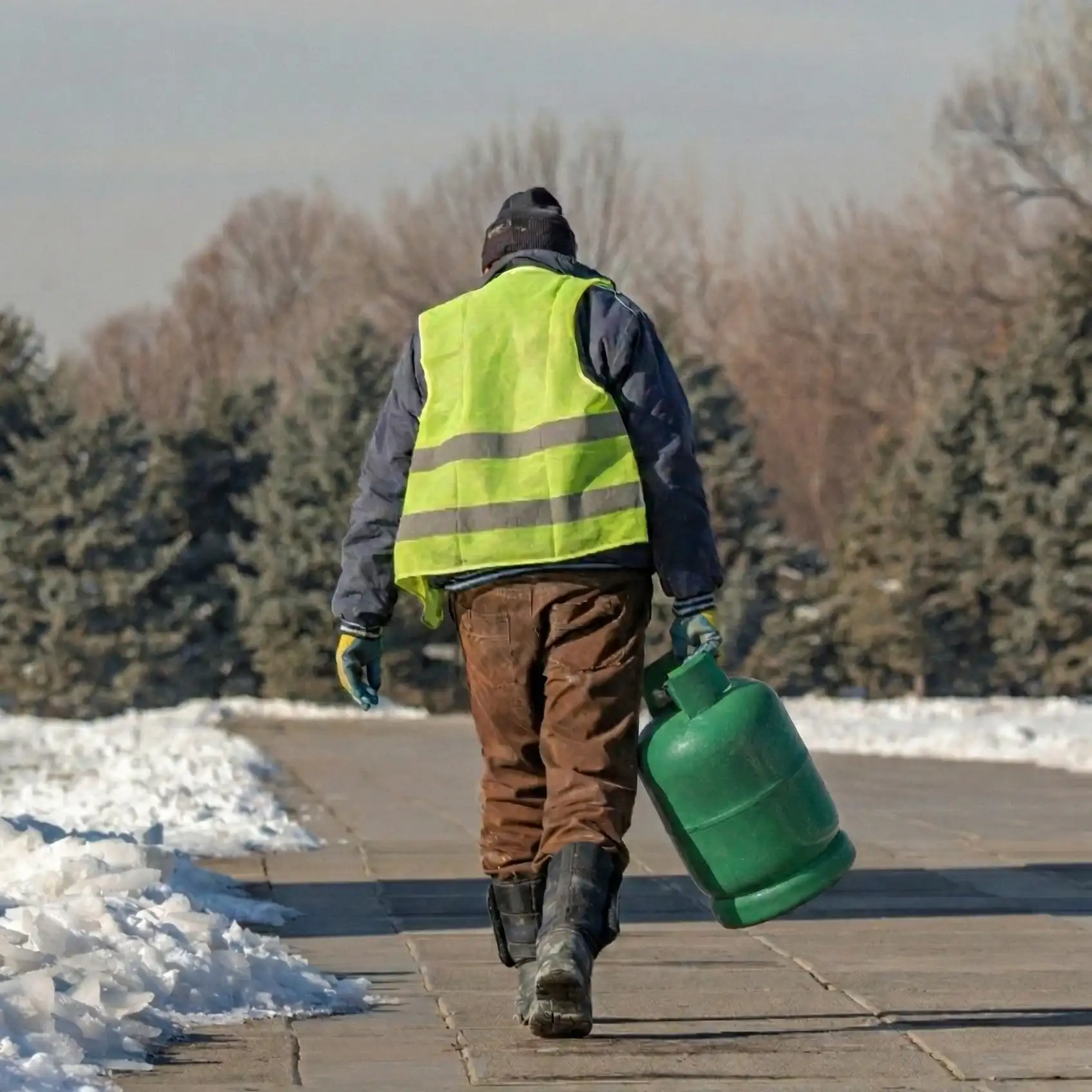 Un ouvrier transportant une bouteille de propane à l'extérieur, par temps neigeux.