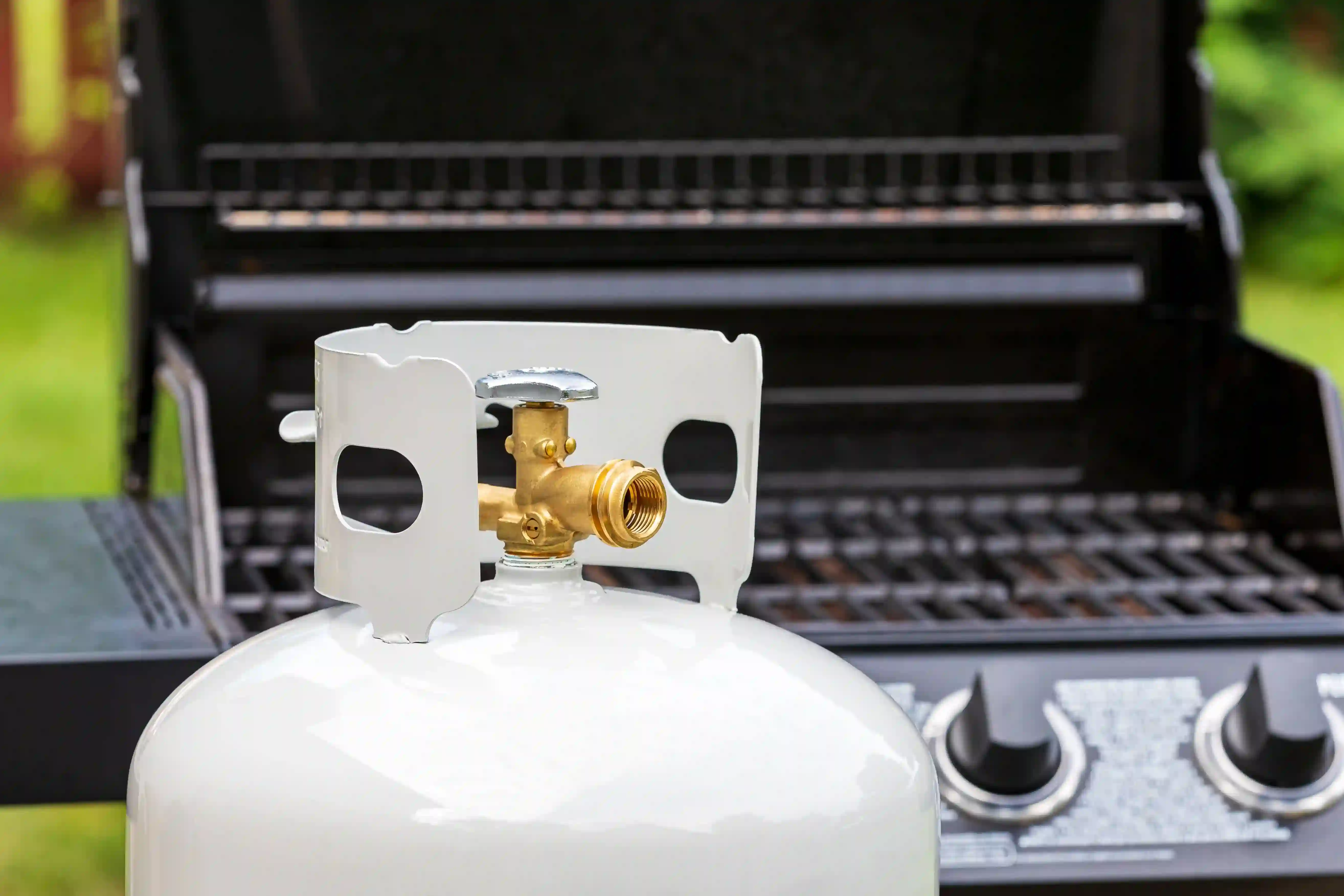 Une bouteille de propane devant un barbecue à gaz d'extérieur.