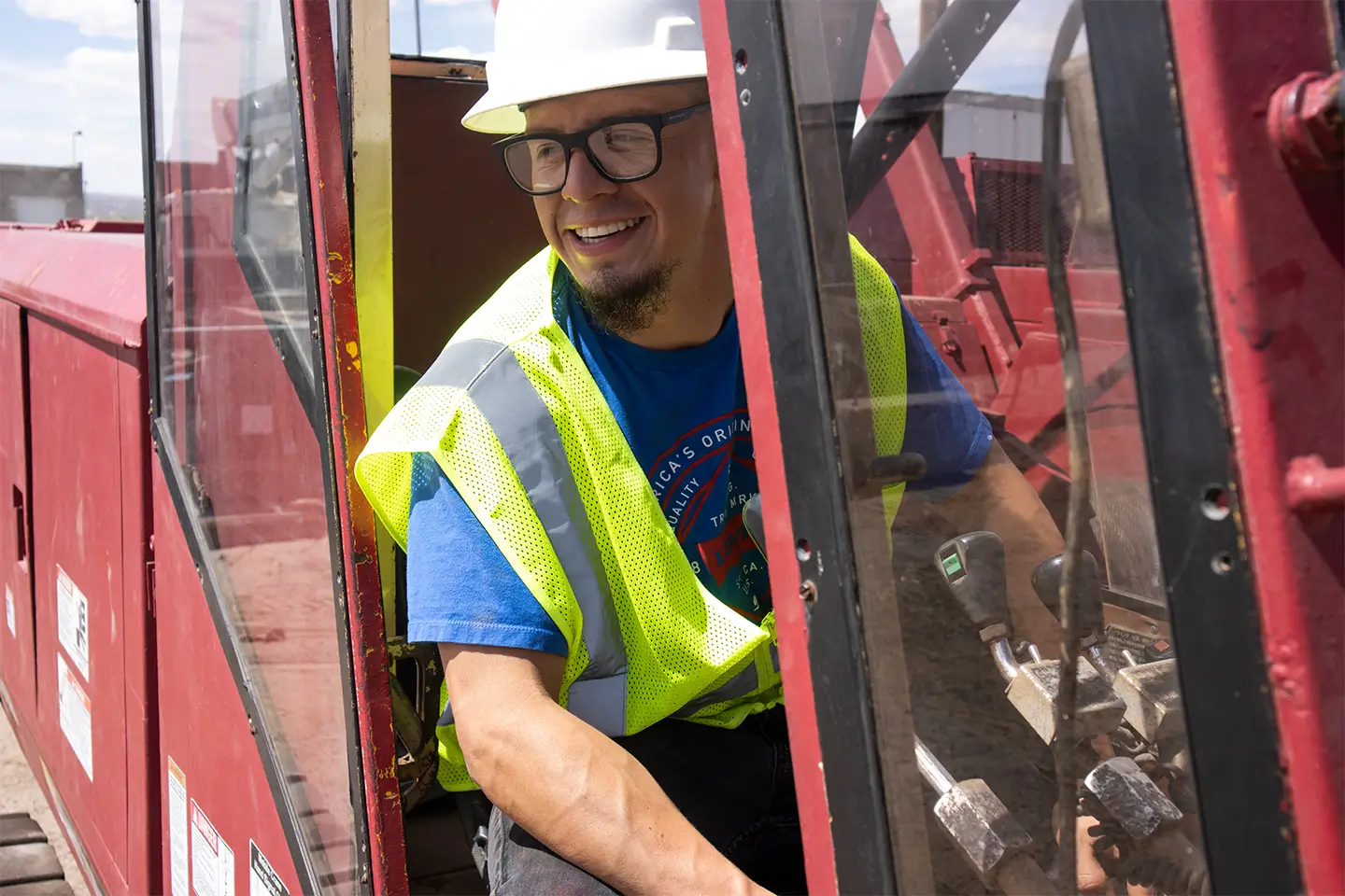 Crane operator trainee wearing a hard hat and safety vest smiling inside the cab of a red crane during hands-on training.