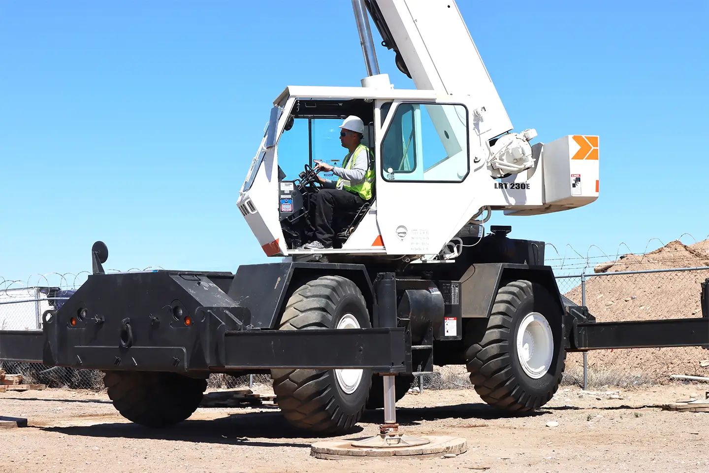Crane operator student in a white cab operating a mobile crane with stabilizers extended during outdoor training.