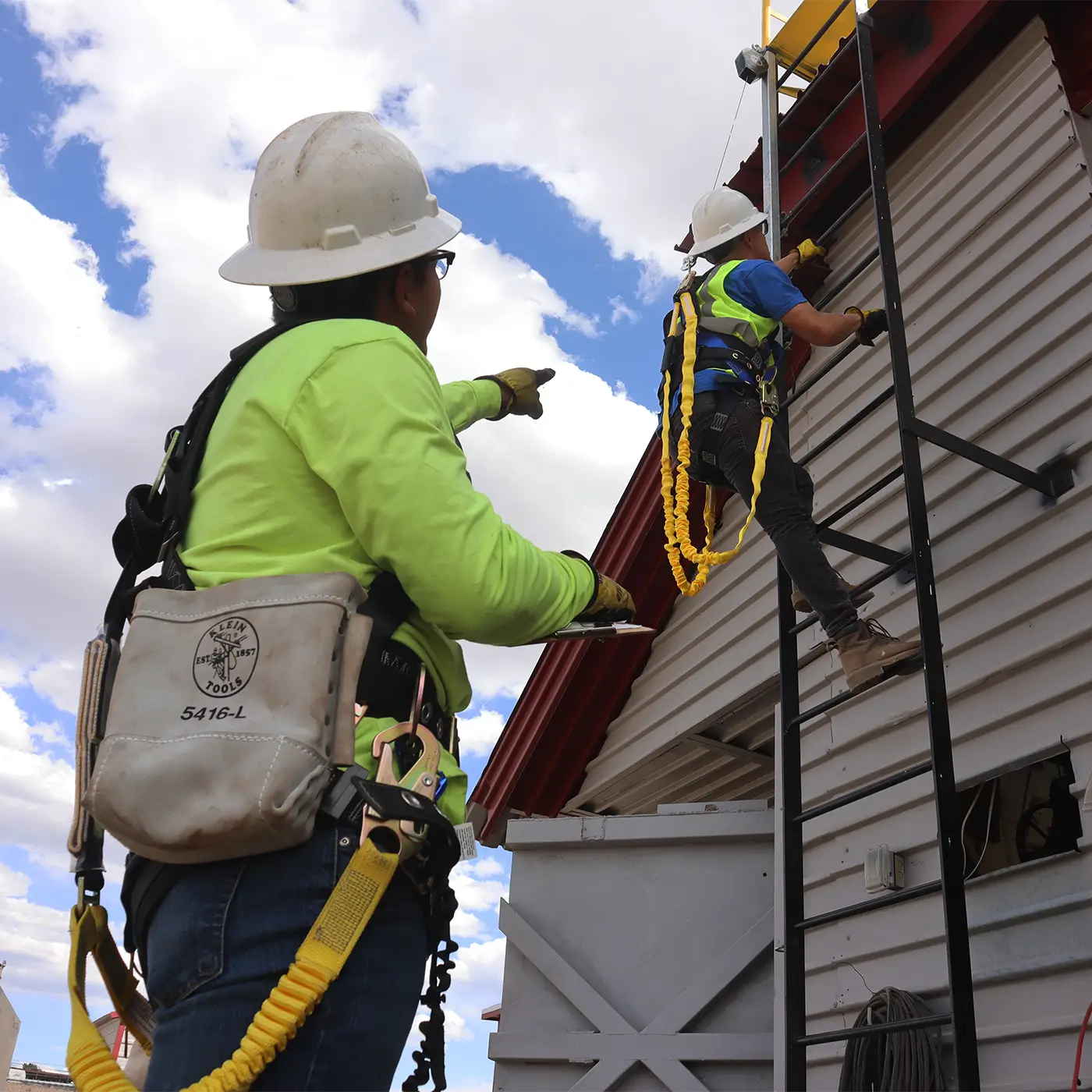 Paradise Crane instructor guiding a trainee using fall protection equipment while climbing a fixed ladder during workplace safety training.