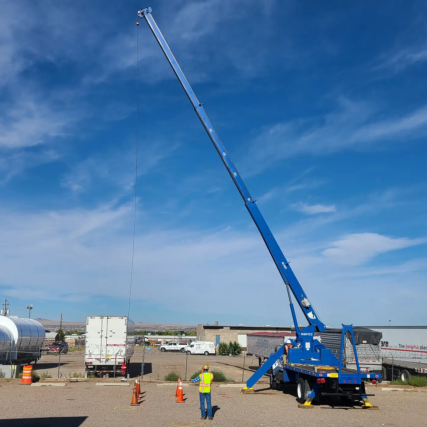 Crane operator trainee working with a blue mobile crane during outdoor training while an instructor observes from the ground.
