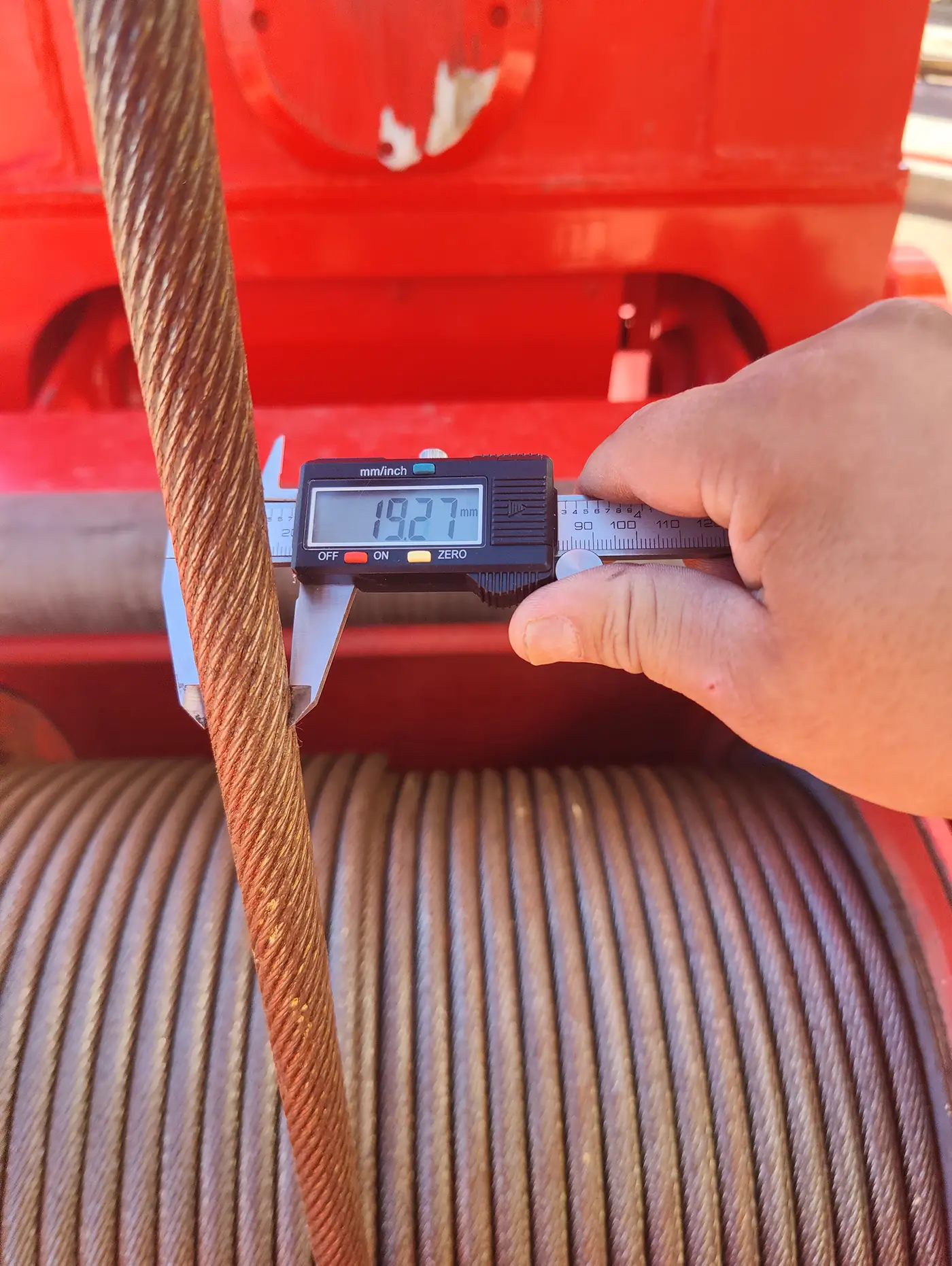 Close-up of crane wire rope being measured with digital calipers during safety inspection.