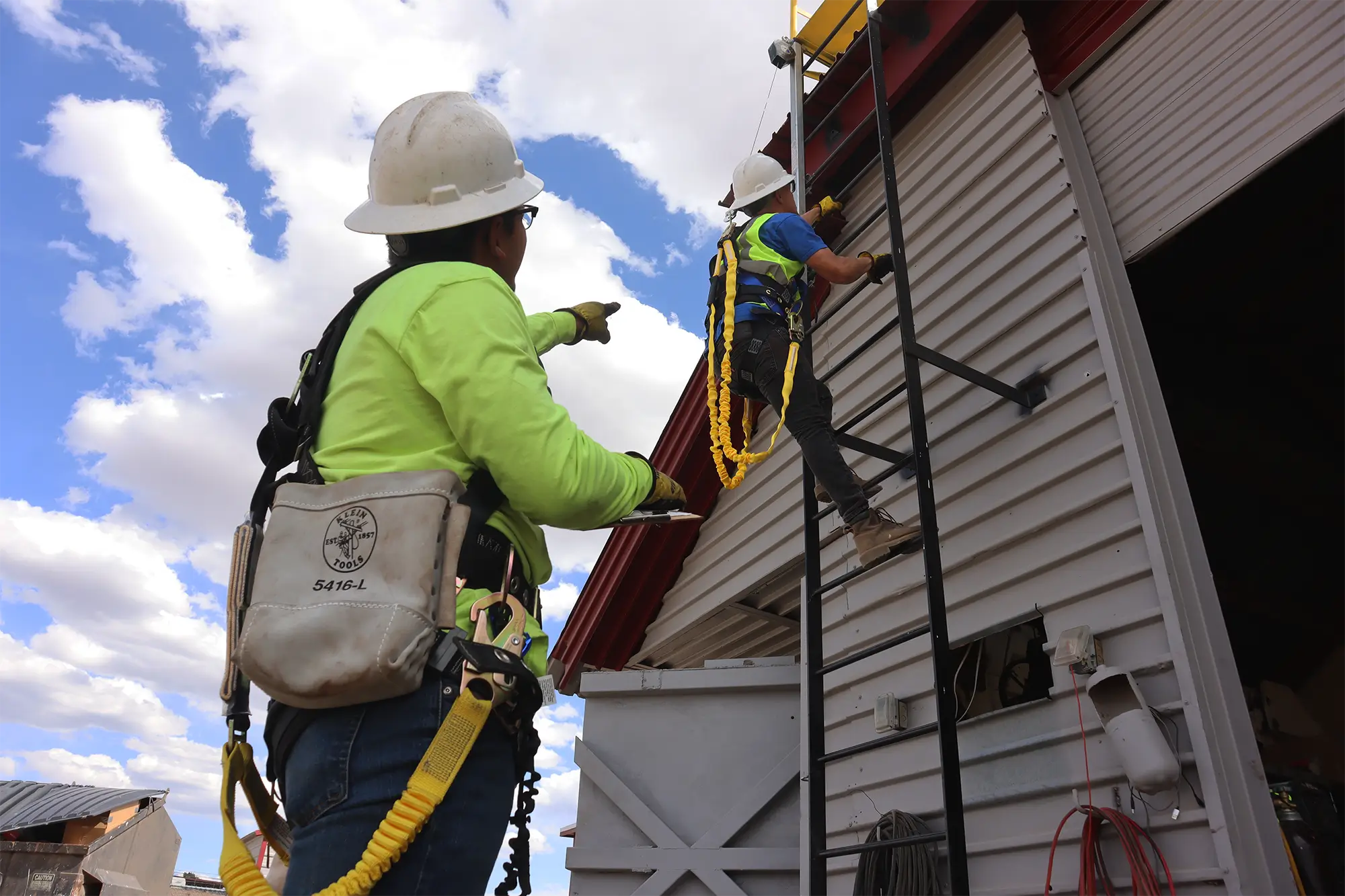 Instructor supervising a student climbing a fixed ladder with fall protection harness during safety training in Albuquerque.