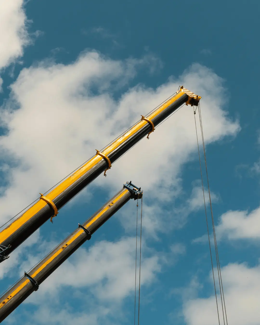 Two yellow mobile crane booms extended into the sky during certification training exercises.