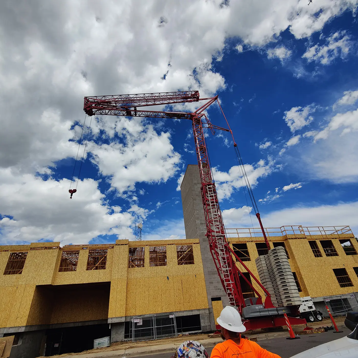 Red telescopic crane lifting materials at a commercial construction site under blue skies.