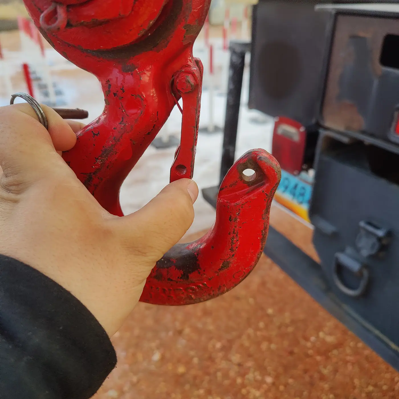 Close-up of a red crane hook during inspection showing wear and missing latch, used in crane safety training.