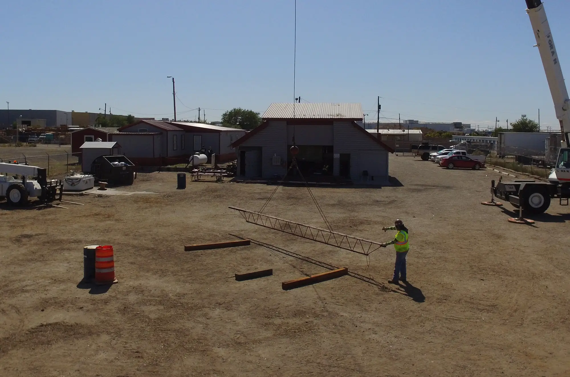 Lift director guiding crane operators during assembly of a lattice boom section at a training yard.