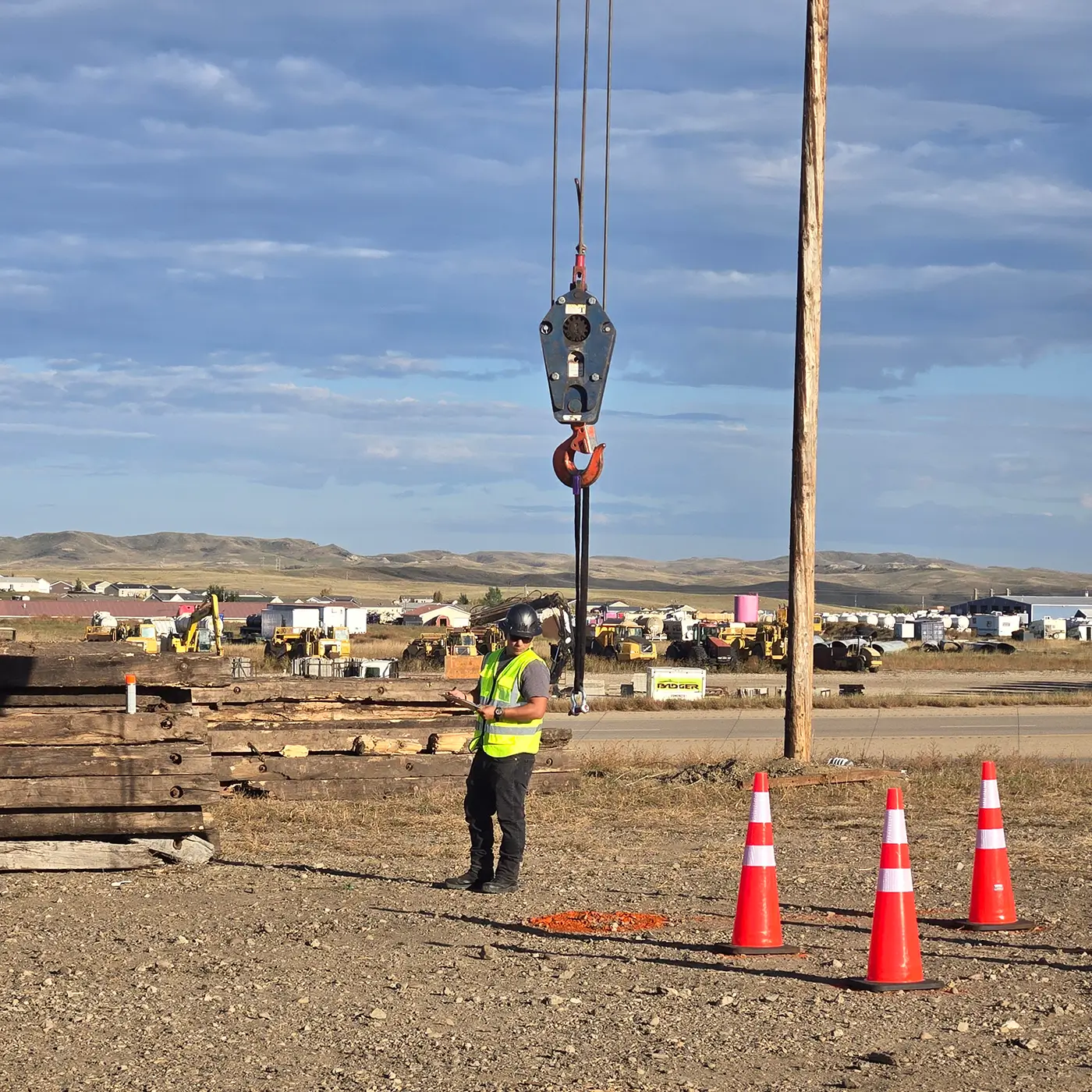 Crane signal person directing a lift with load hook during operator training session on construction site.