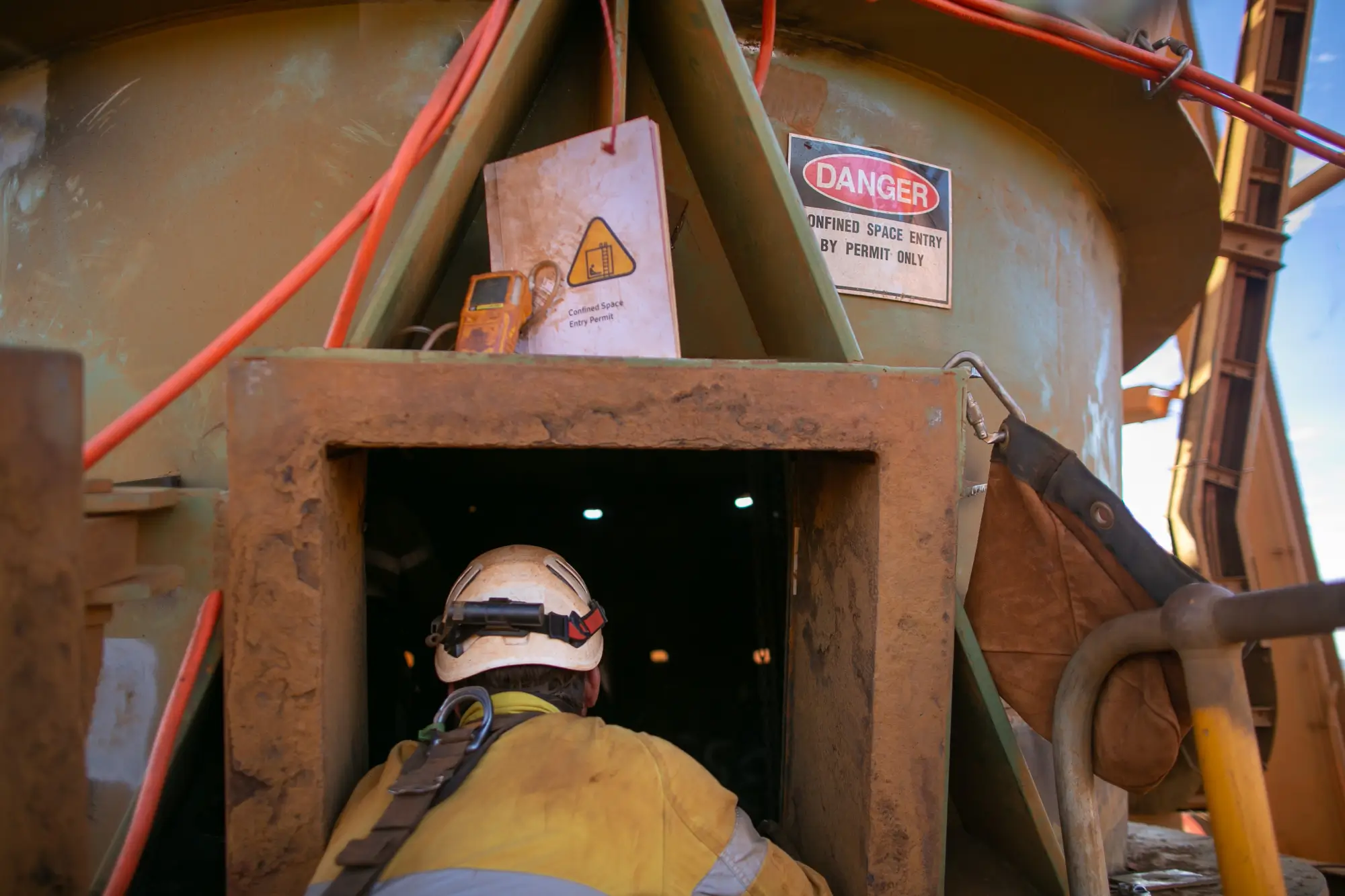 Worker entering confined space with safety harness and gas monitor during confined space entry training.