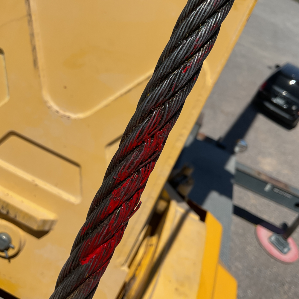 Close-up of a crane wire rope with red damage marker applied during inspection for wear and safety compliance.