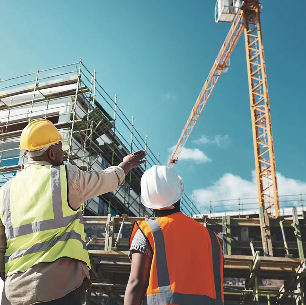 Construction site supervisor and safety trainee conducting risk management assessment near an active crane operation.