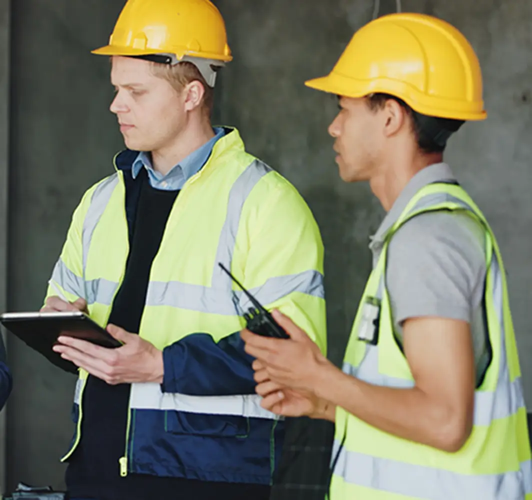 Safety inspectors reviewing construction site operations and performing a risk assessment using digital tools and communication equipment.