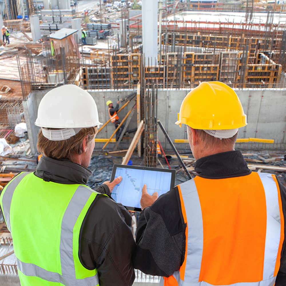 Construction managers reviewing project plans on a tablet during a due diligence safety assessment at an active jobsite.