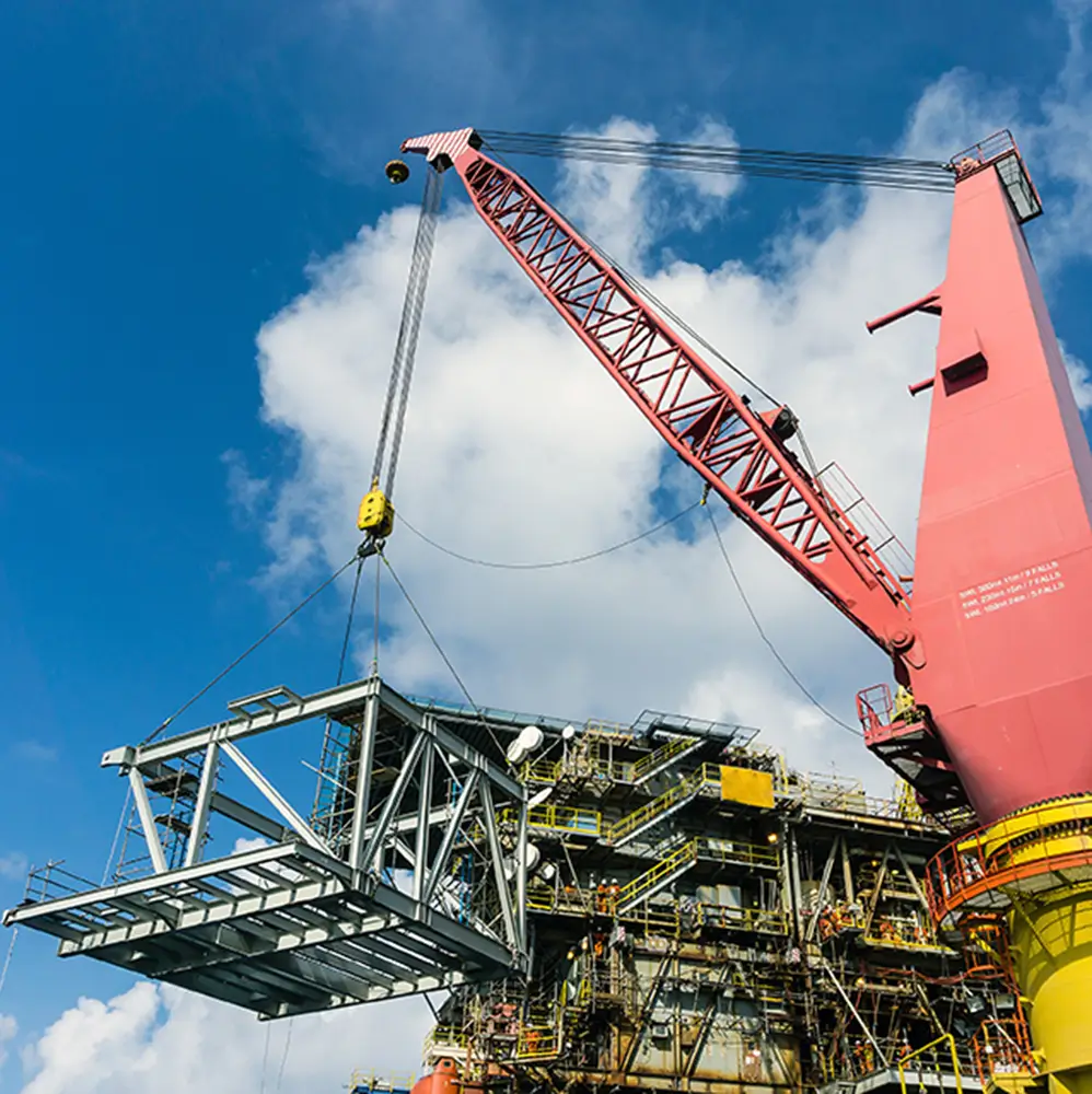 Large crane performing a specialized heavy lift rigging operation on an industrial worksite under clear blue skies.