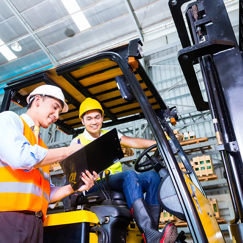 Forklift operator receiving hands-on safety training and certification guidance from an instructor inside a warehouse.