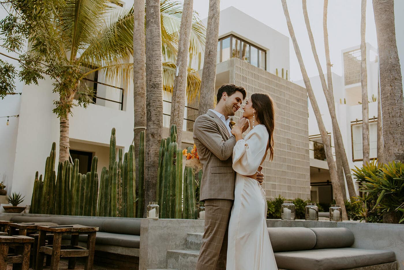 Romantic couple embracing outdoors at a modern tropical villa with tall palm trees, cacti, and white architecture in the background