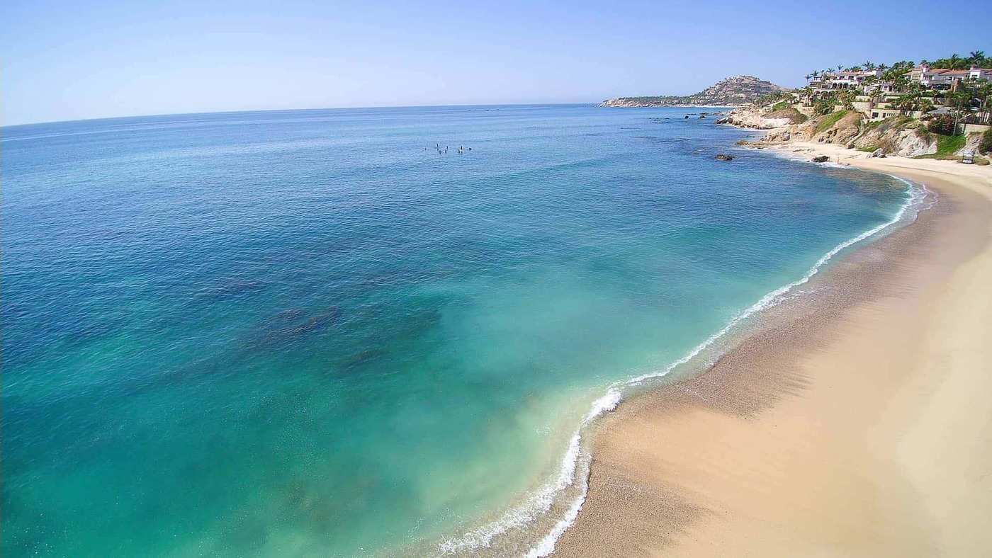 Scenic aerial view of a pristine sandy beach with turquoise ocean waves and coastal villas in Los Cabos, Mexico